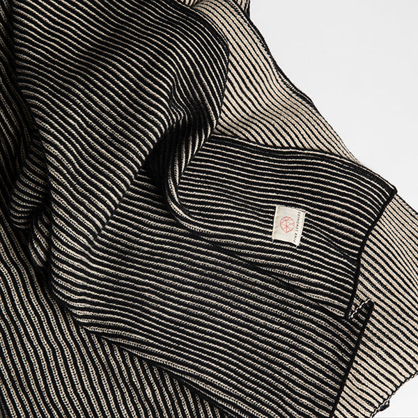 Close-up of a black and white striped throw with the Pink Lemonade brand label pictured a light gray background.