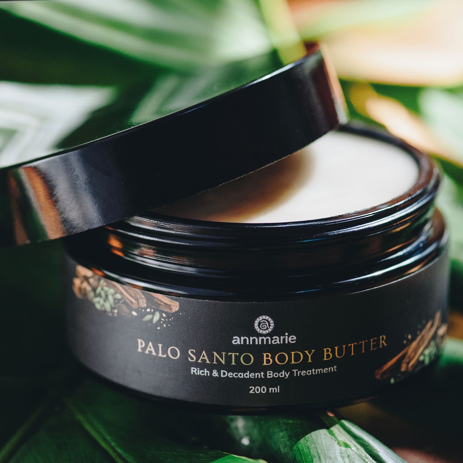Open jar of Palo Santo body butter with a tropical leaf background