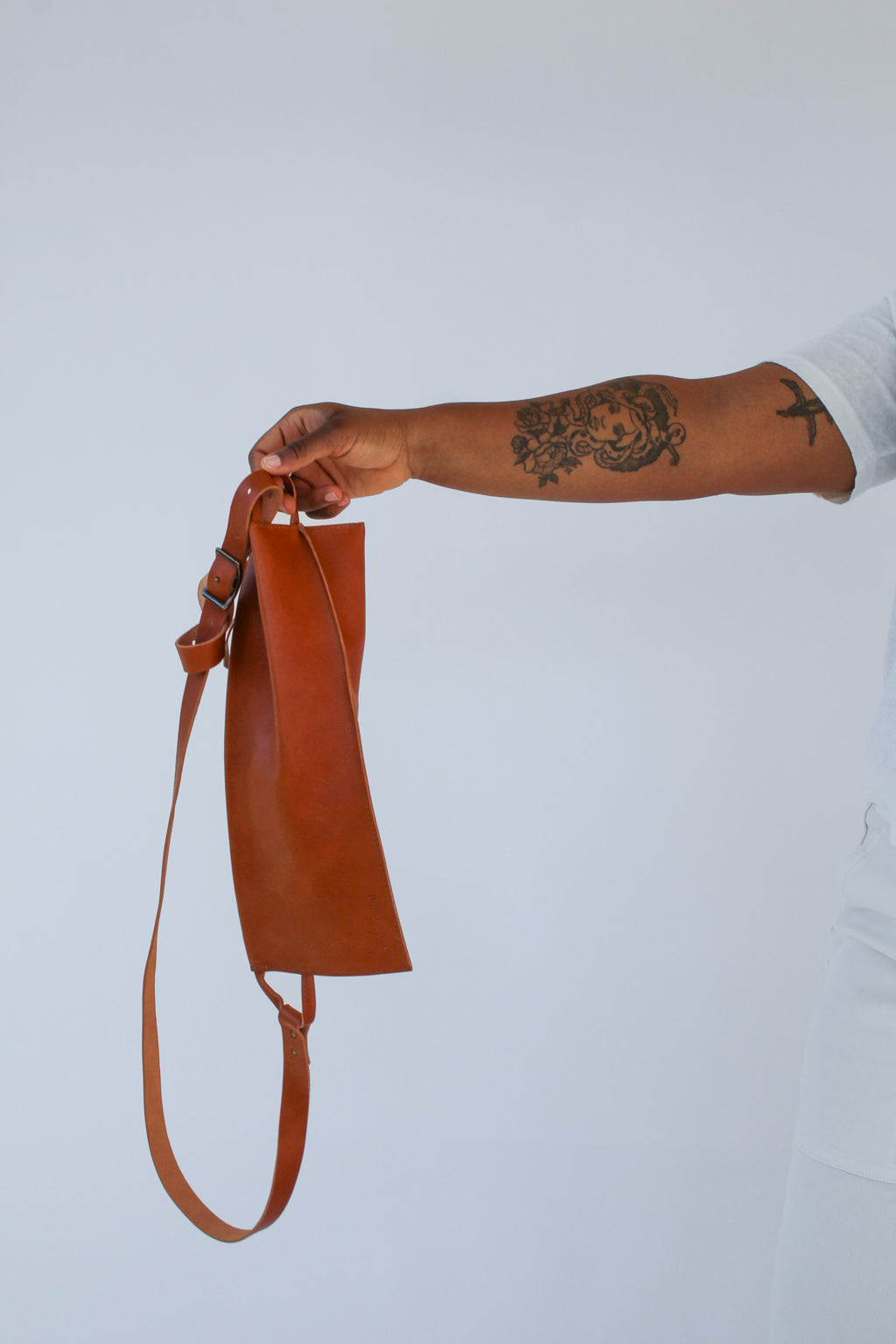 A woman holds out a light brown chestnut leather fanny pack shoulder bag against a white background.
