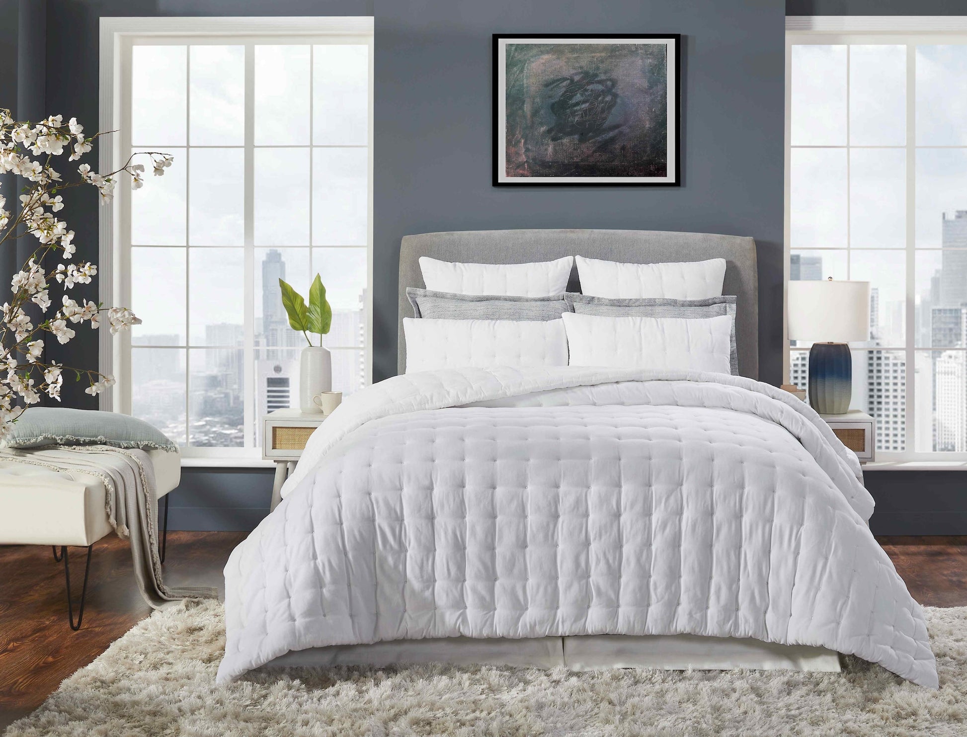 QT-353-11096_1|Modern white quilted bedding set on a king-size bed in a stylish bedroom with large windows overlooking a city skyline.