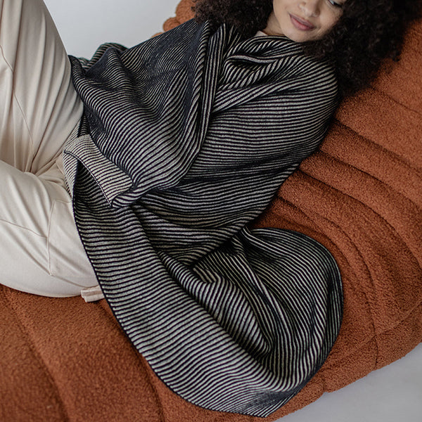 Woman laying down on brown bed and wrapped in a black and white ribbed cotton throw blanket.