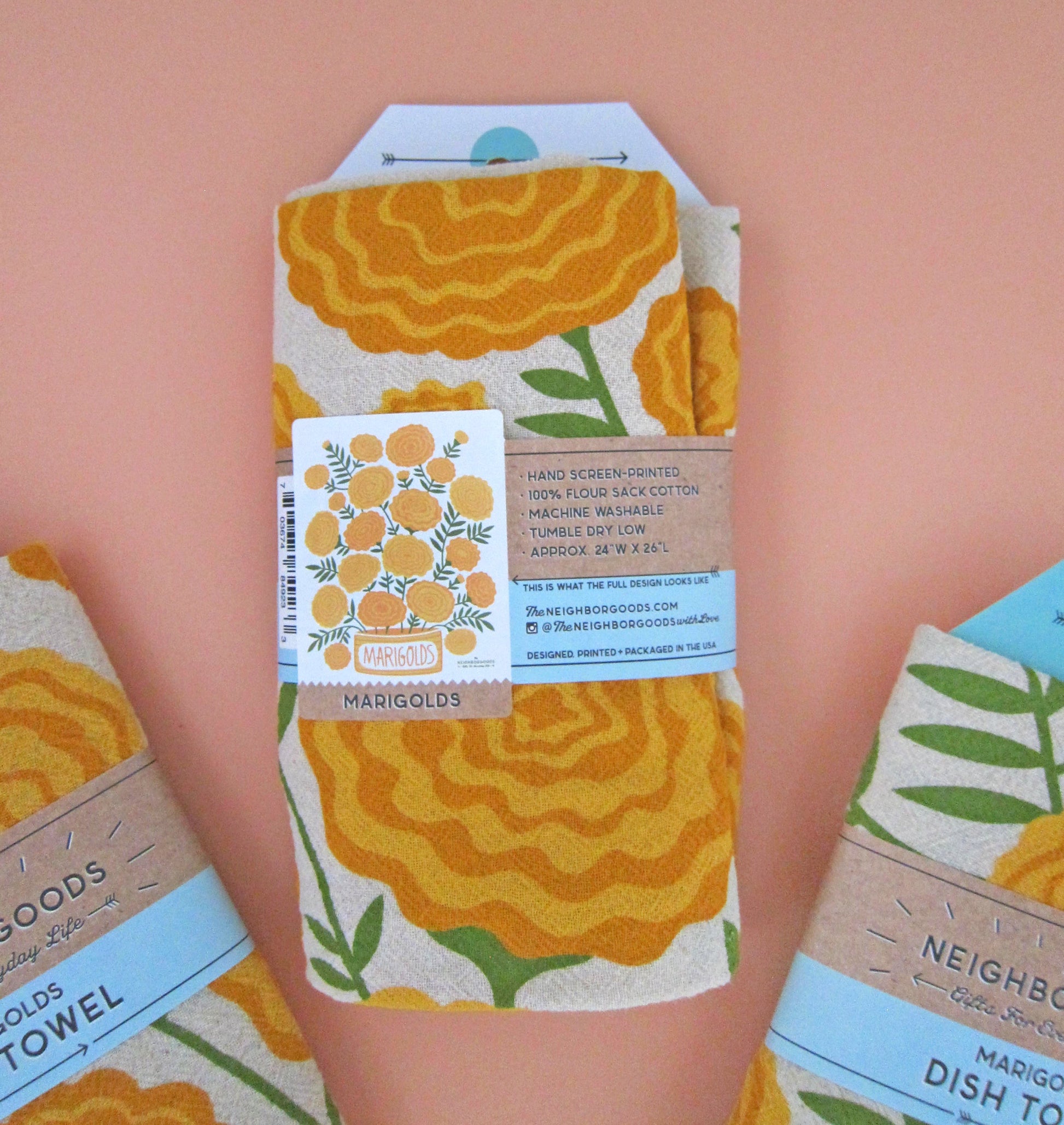 Back view of The Neighborgoods Marigolds dish towel in a ready-to-gift sleeve, showcasing product specifications and an image of the full tea towel.