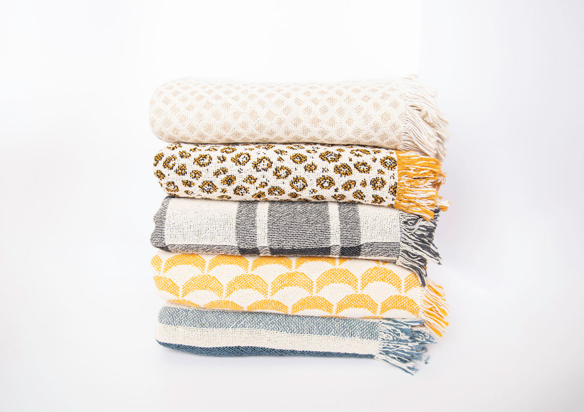 Stack of five Kindly Woven patterned blankets with Sutton Delft coastal stripe at the bottom