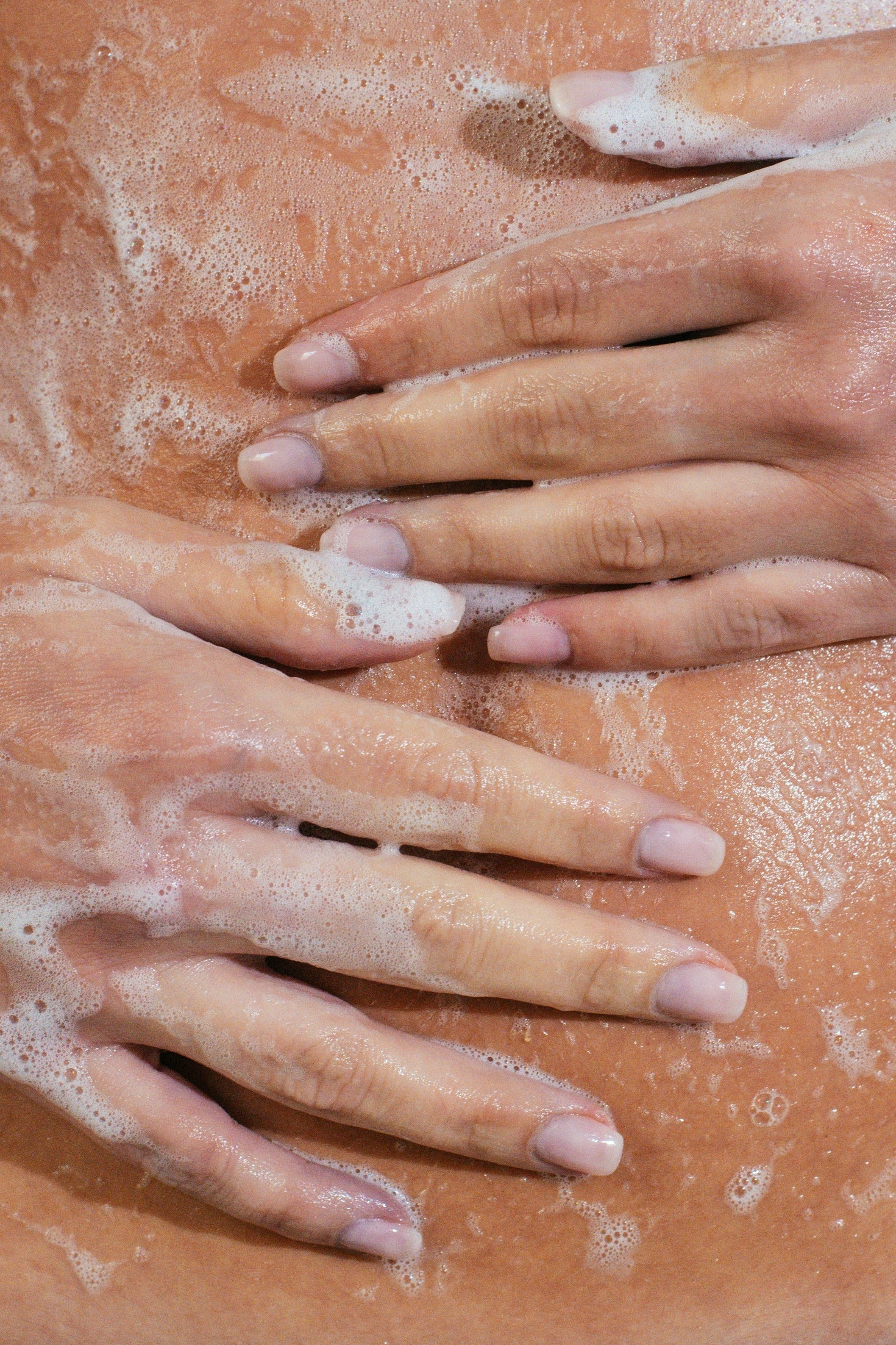 Close-up of woman's hands with soap suds on stomach