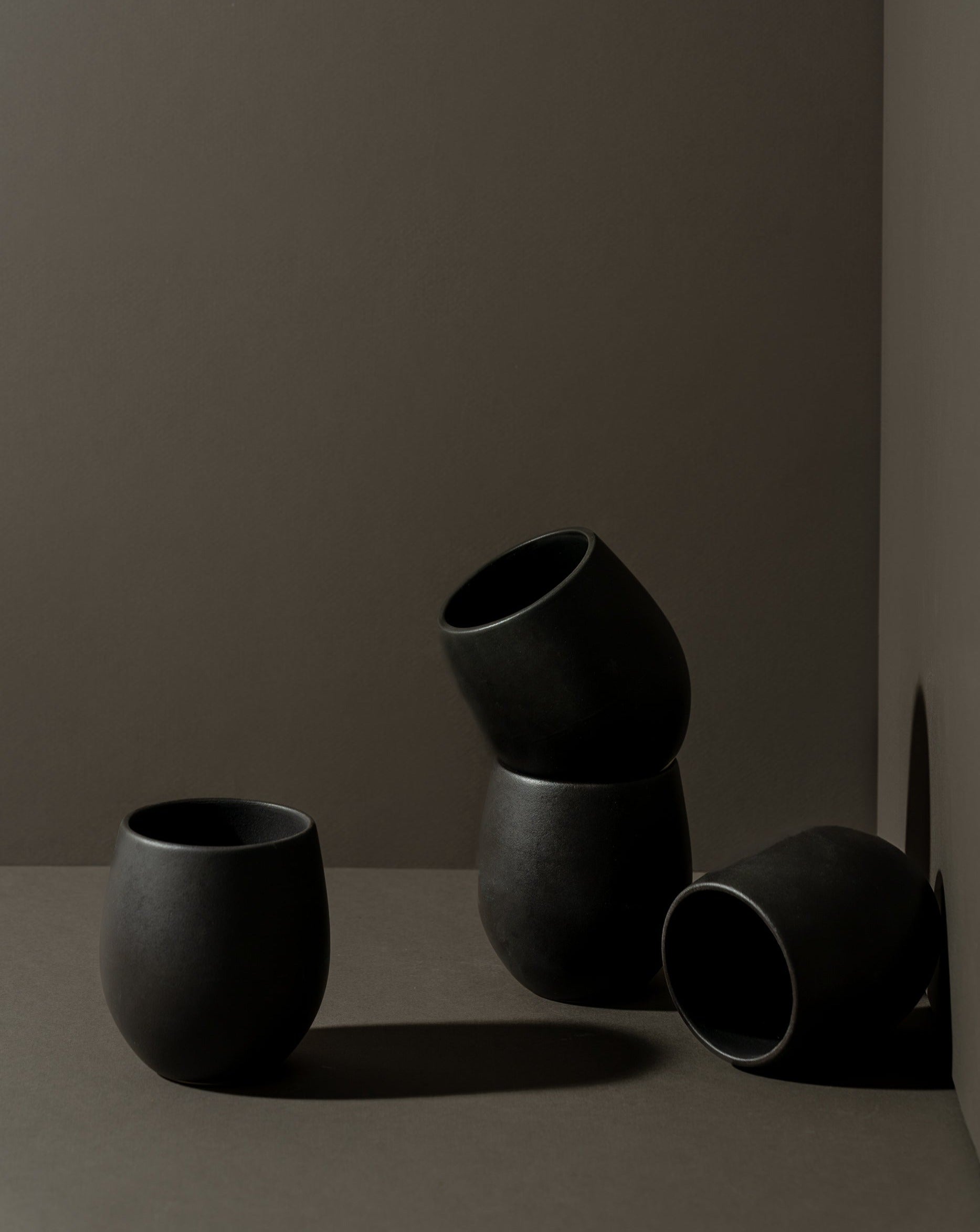 A set of four stoneware coffee cups arranged in a casual manner, with a matte black finish.