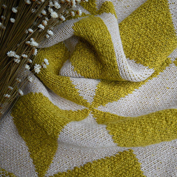 Organic cotton throw with green and white geometric patterns next to dried baby's breath flowers.