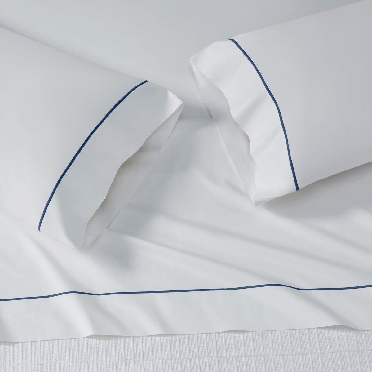 ASP-549-2032_6|Close-up of a white 100% cotton flat sheet corner. Accented with a single navy blue piped decorative border.