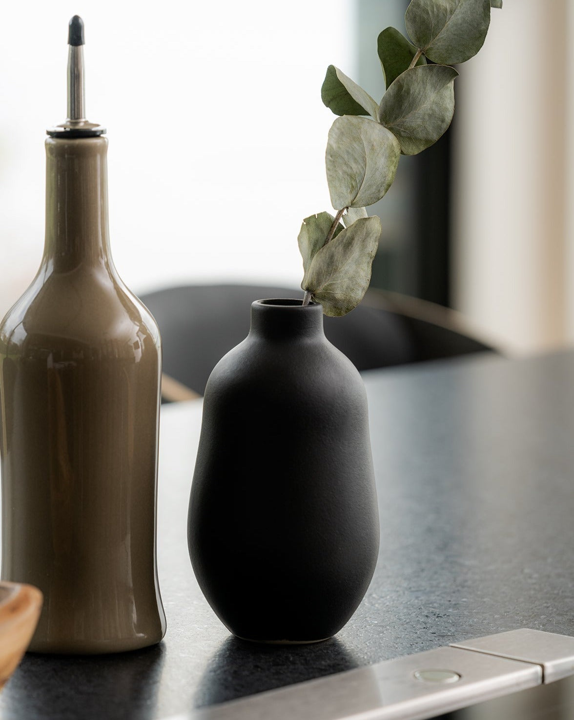 A white stoneware vase with a minimalistic design, placed on a surface and containing a green plant, showcasing its use as a decorative table accessory.