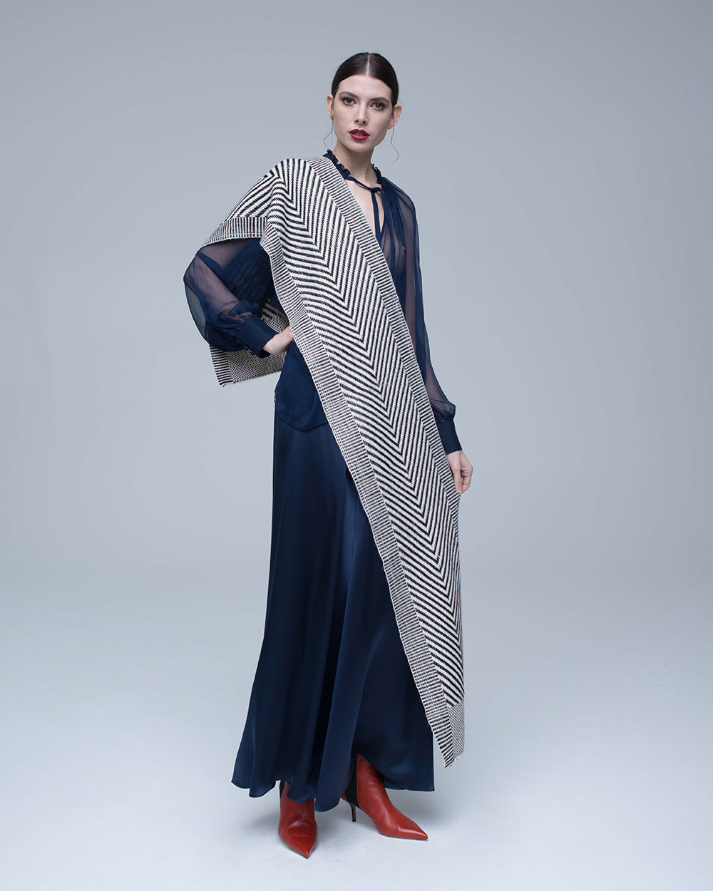 Model wearing a chevron scarf in ivory and black, styled with a navy dress and red boots.