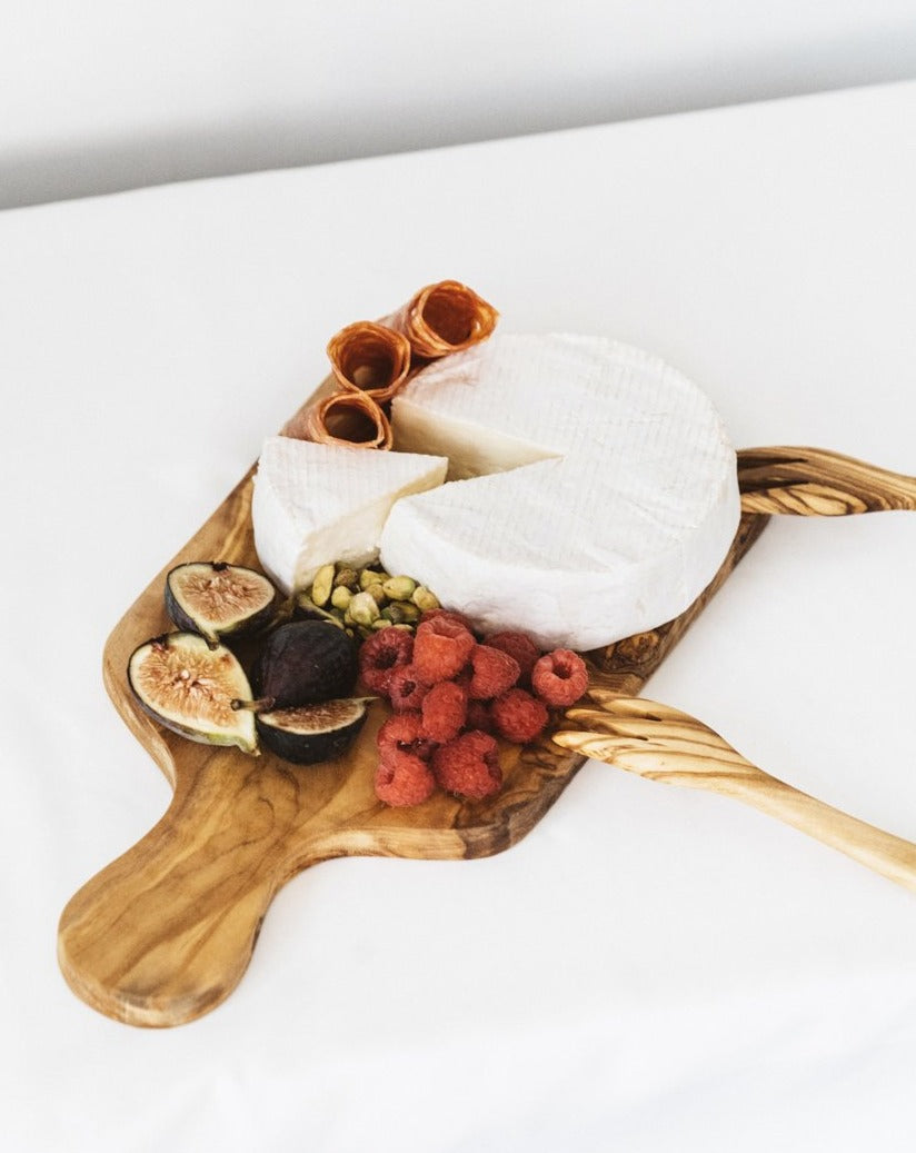 Natural olive wood cheese board with assorted foods and two tapas forks placed on the side