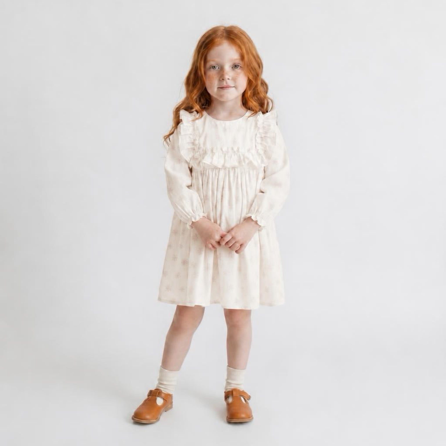 Young girl wearing a white dress with long sleeves on a plain background