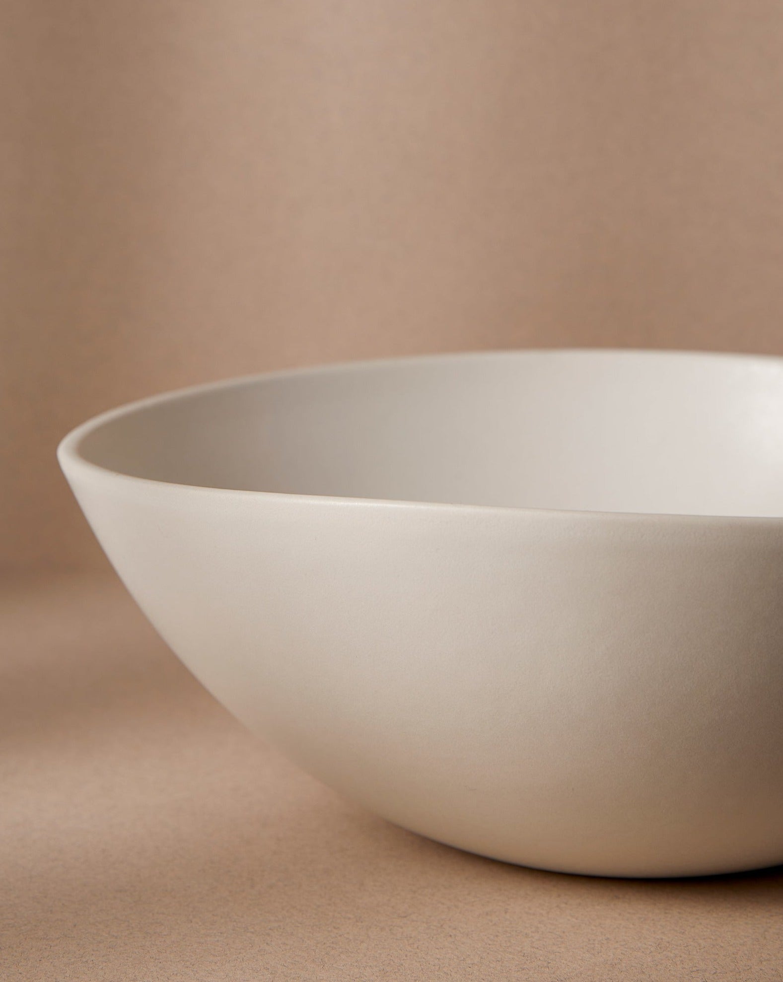 White stoneware serving bowl, partially shown in frame, displayed against a cream background.