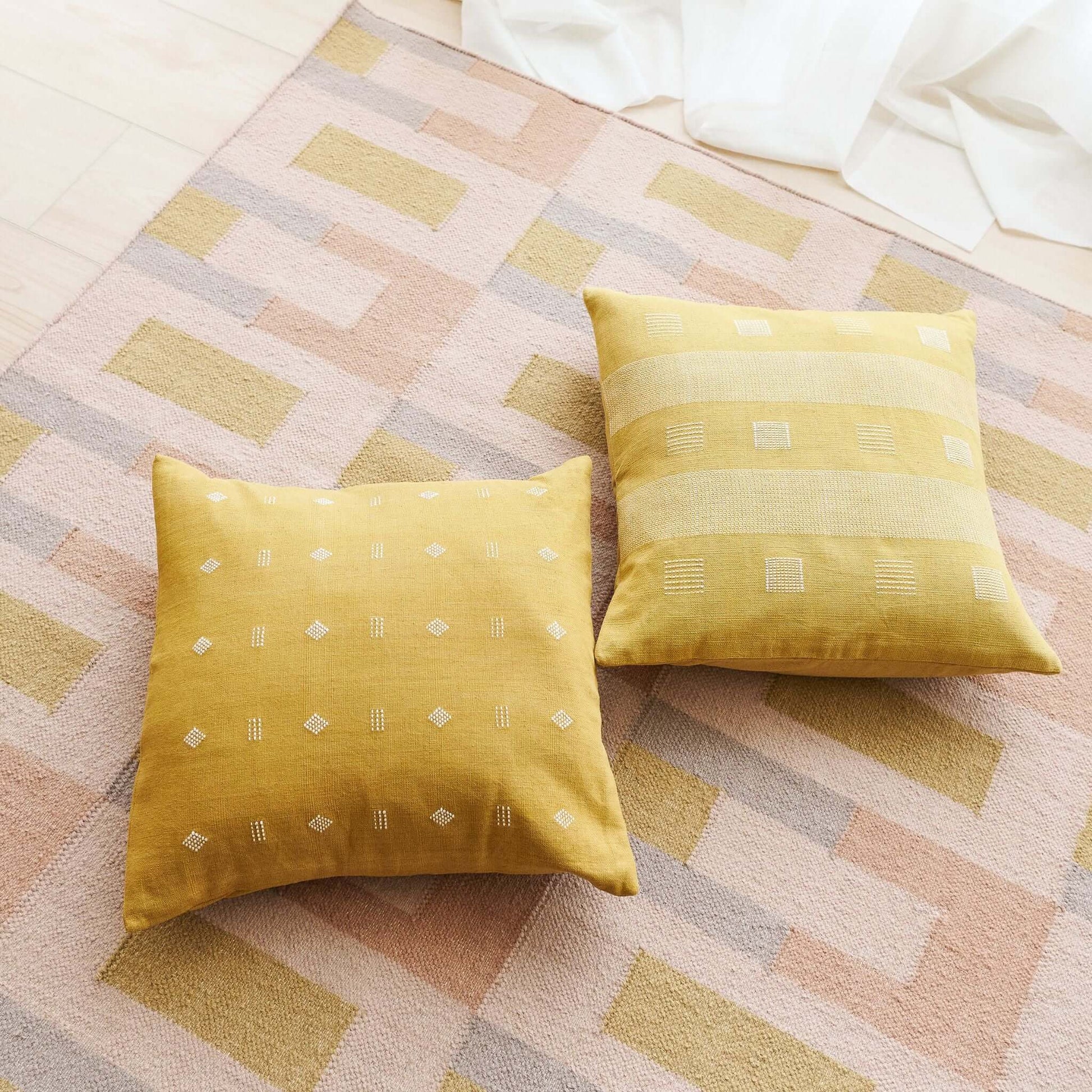 Nira Ochre Hand Spun Organic Cotton Handloom Pillow on a stylish rug, showcasing unique handwoven texture and undyed yarn details.