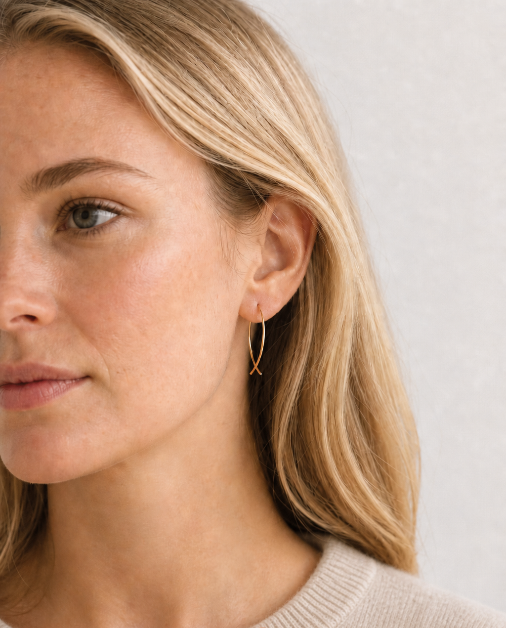 Close-up of a woman wearing gold hoop earrings against a neutral background