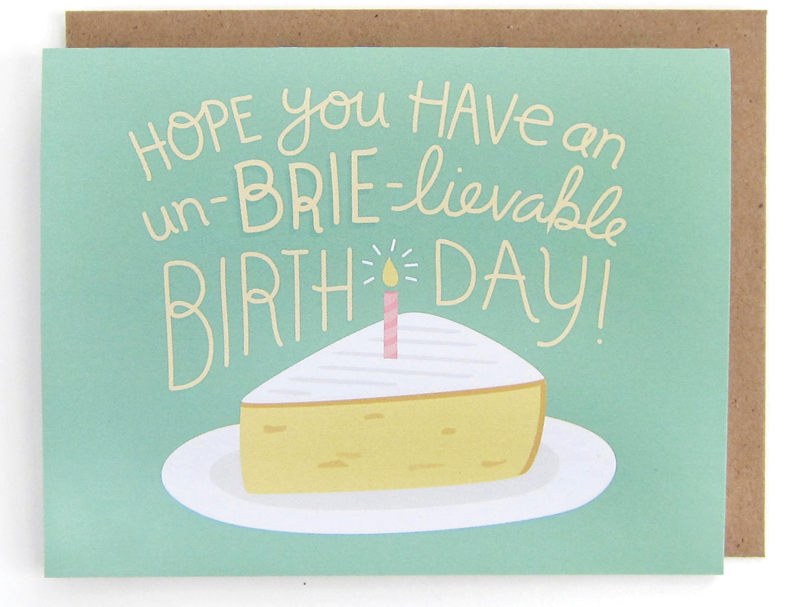 Light green card that pictures a slice of brie cheese with a candle, featuring the phrase "Hope you have an un-brie-lievable birthday!" with a brown envelope
