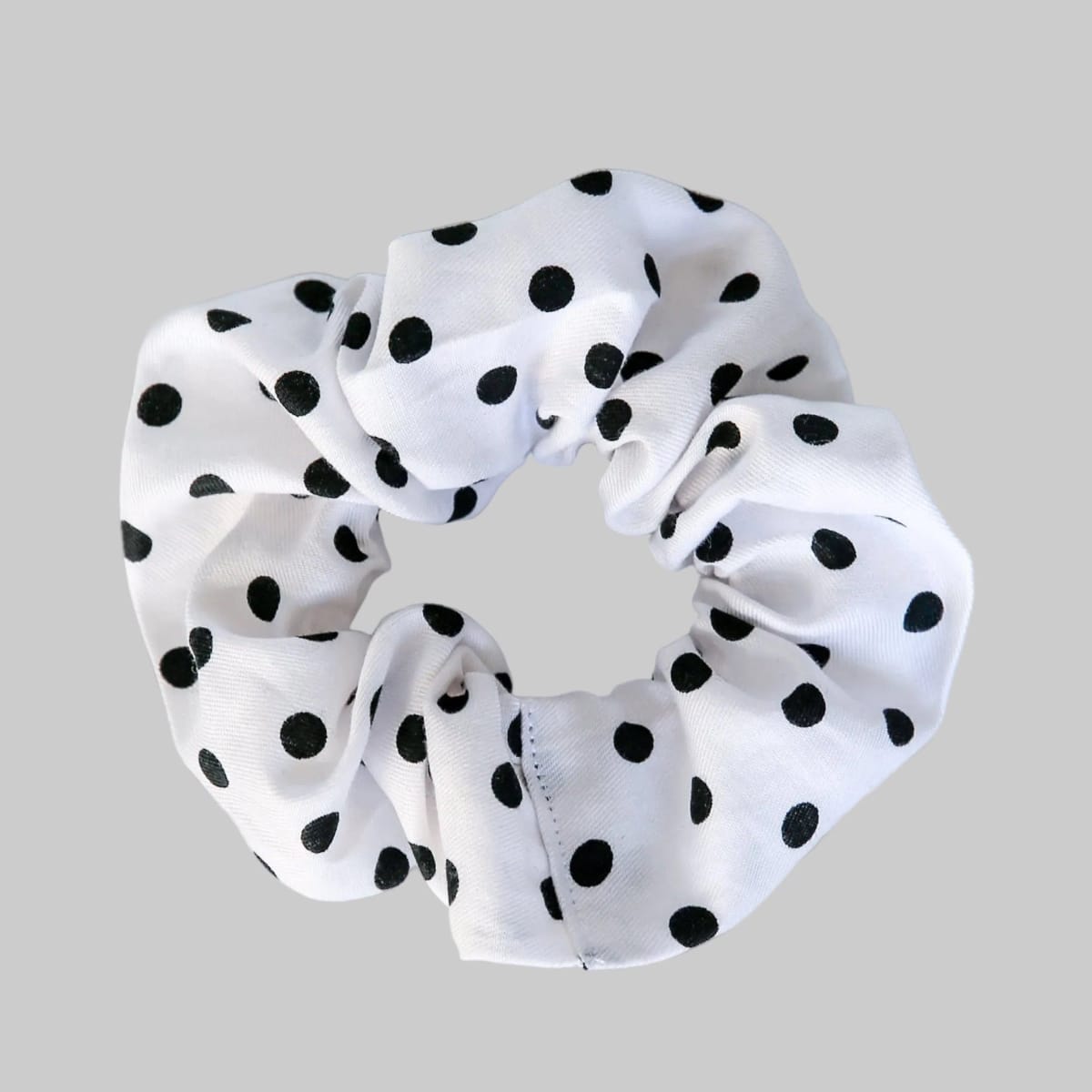 White scrunchie with black polka dots on a gray background