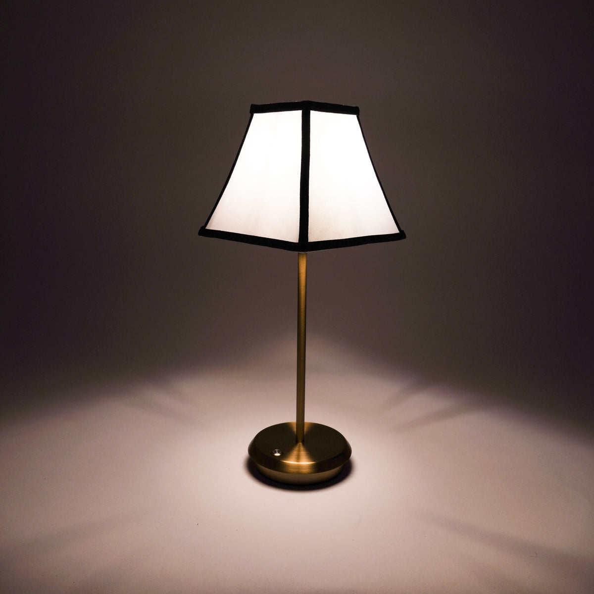 Noir & Pearl cordless table lamp with white shade, black trim and gold base illuminated.