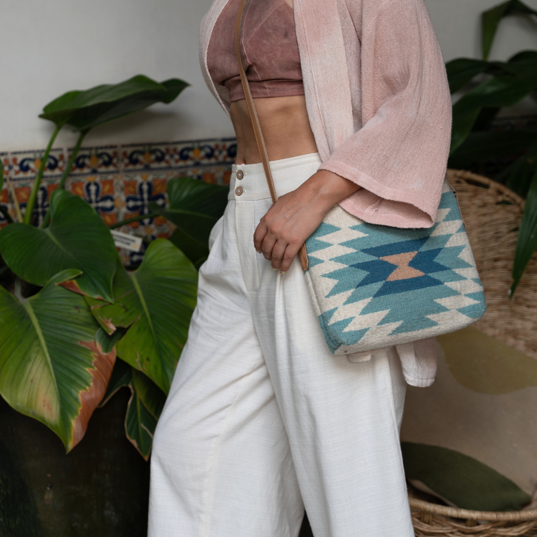 Woman carrying handwoven crossbody bag with abstract Zapotec diamond design in soft spring tones; features adjustable leather strap and two internal pockets for daily essentials