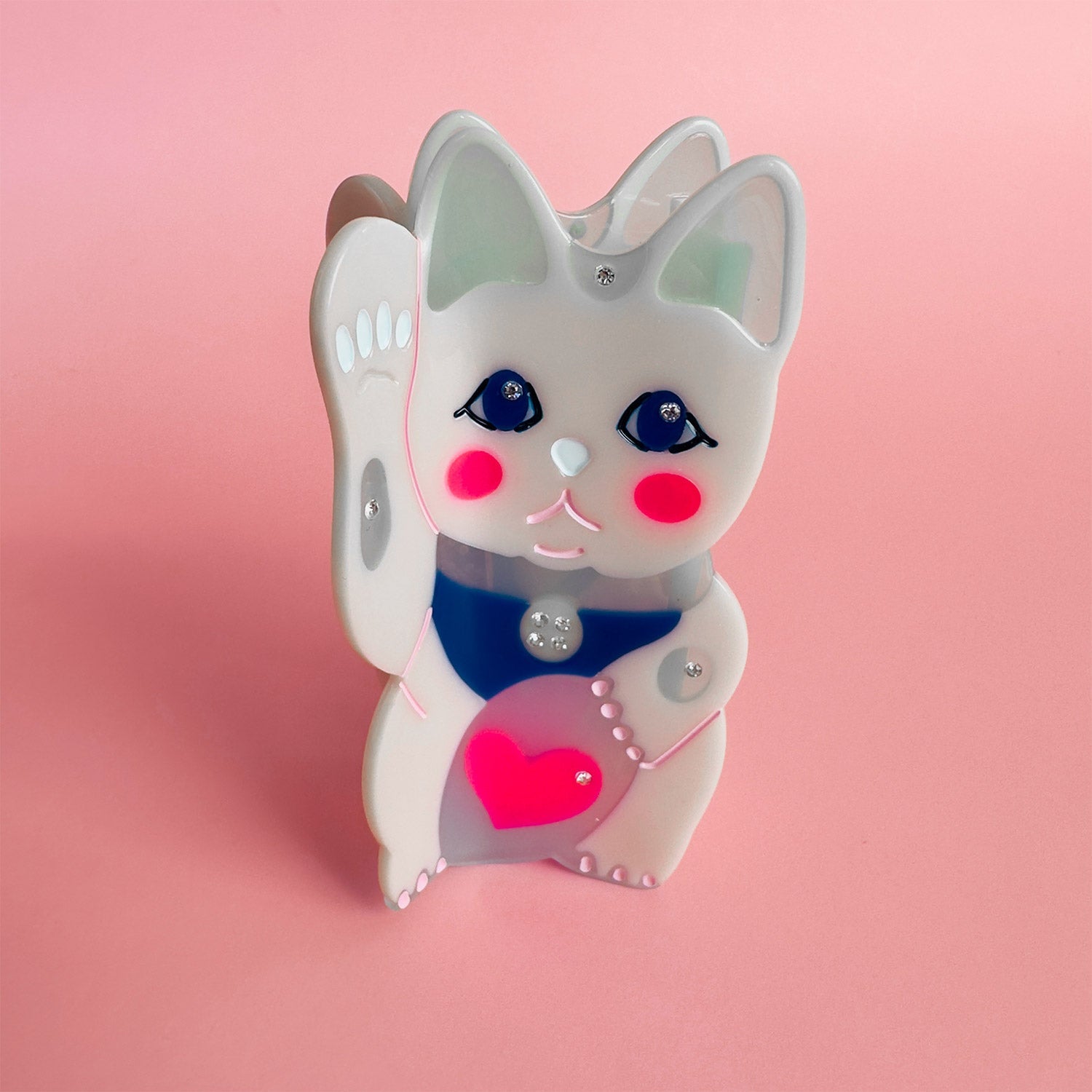 A maneki-neko white cat hair claw with a pink heart from Centinelle. Handmade on cellulose acetate, with splice technique, exquisite miniature details and crystals, that are tied directly to its value and make them unique and special. 