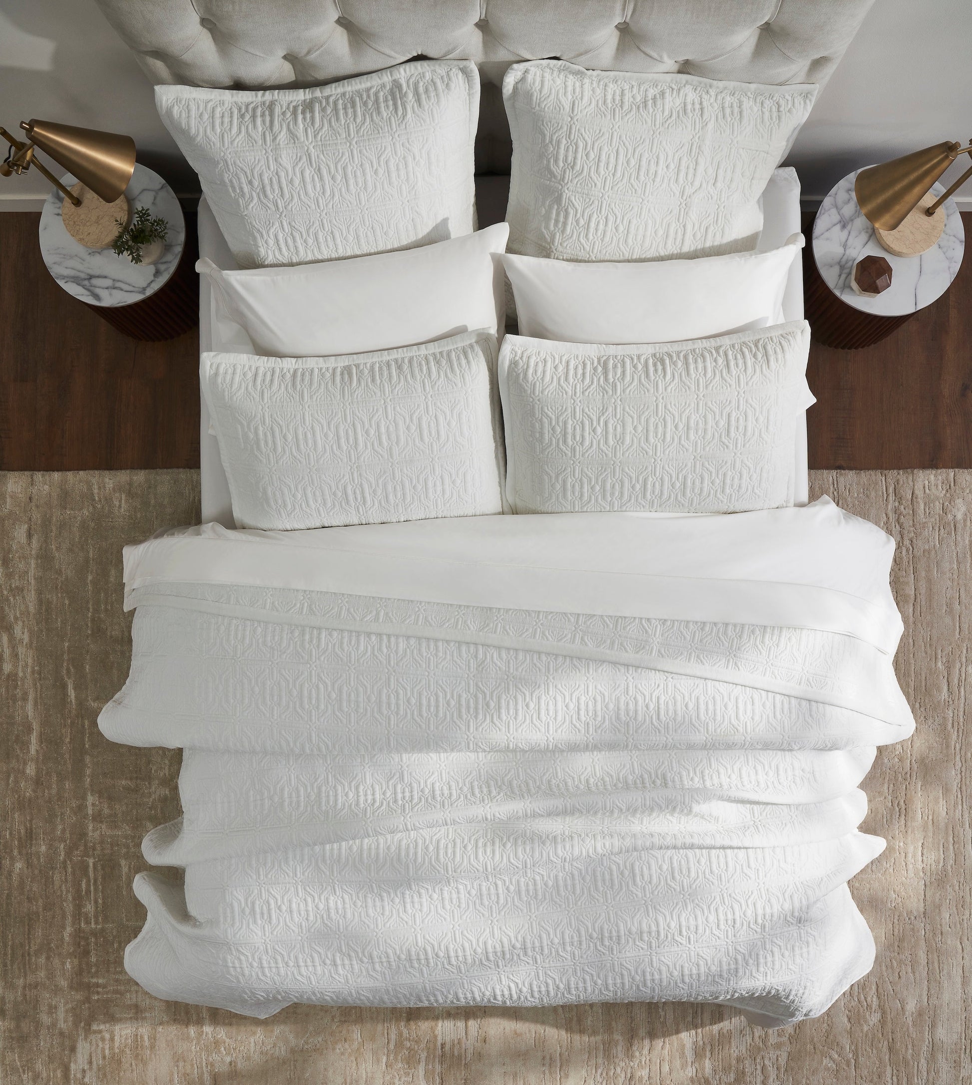 QT-376-11096_4|Overhead view of a bed showcasing a pristine white patterned quilt and full bedding set, emphasizing geometric texture and style.