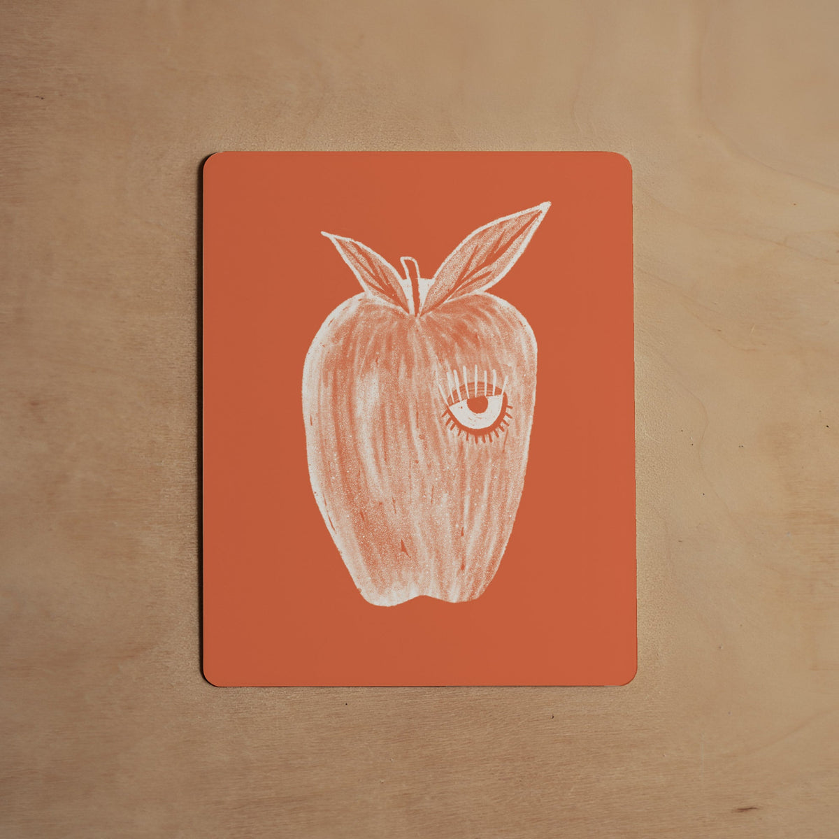 Card with a white apple illustration on an orange background, placed on a wooden surface.