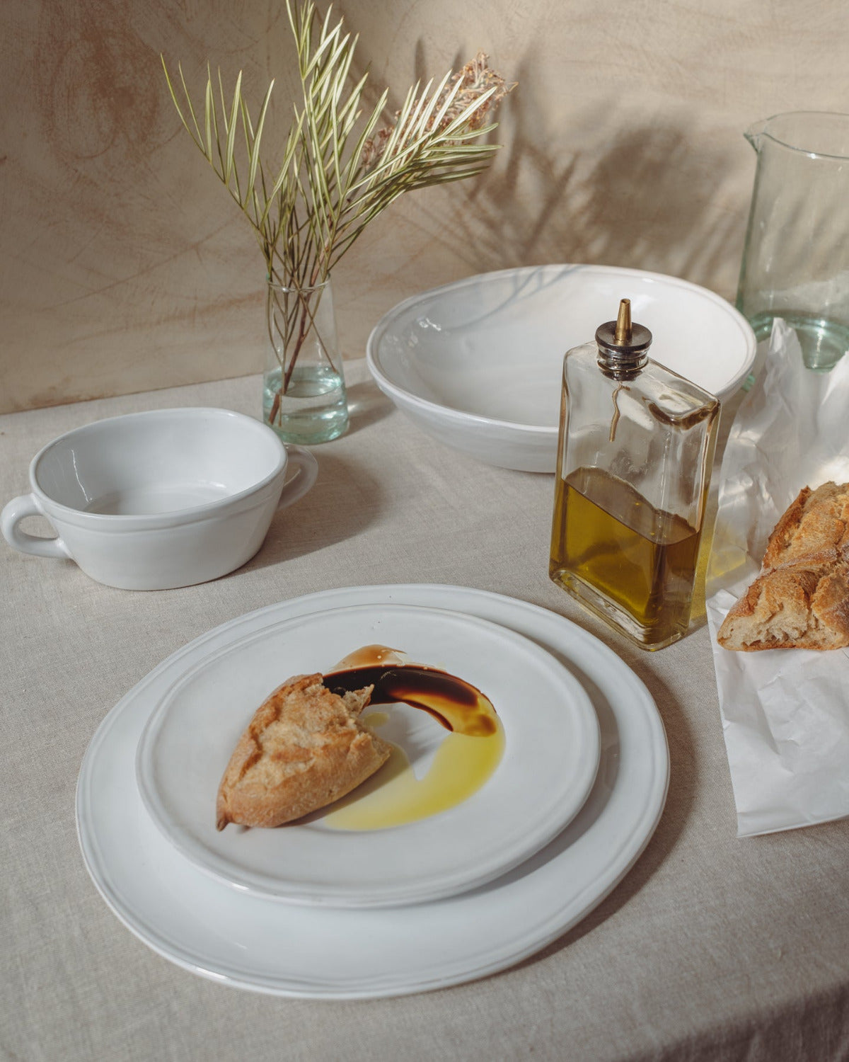 Table setting with a plate of food, olive oil bottle, and bread on a neutral background