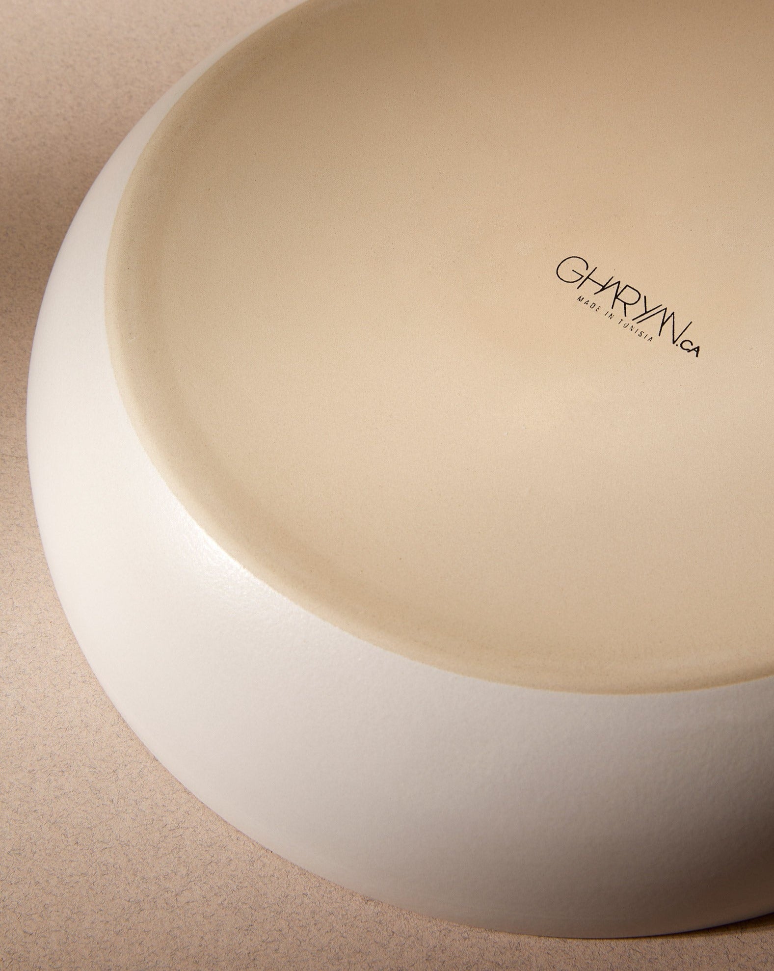 An off-white stoneware shallow serving bowl placed upside down on a plain white background, showing the “GHARYAN” branding on the base.
