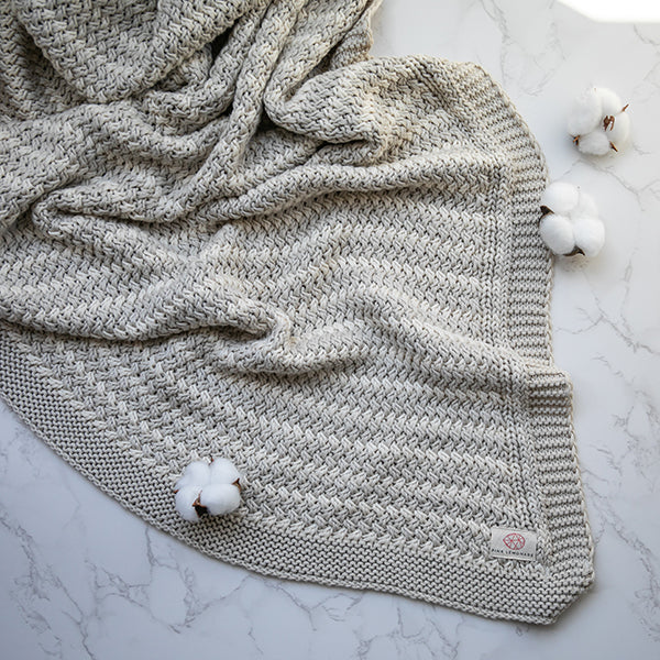 Silver knitted cotton throw blanket with cotton balls on a marble surface