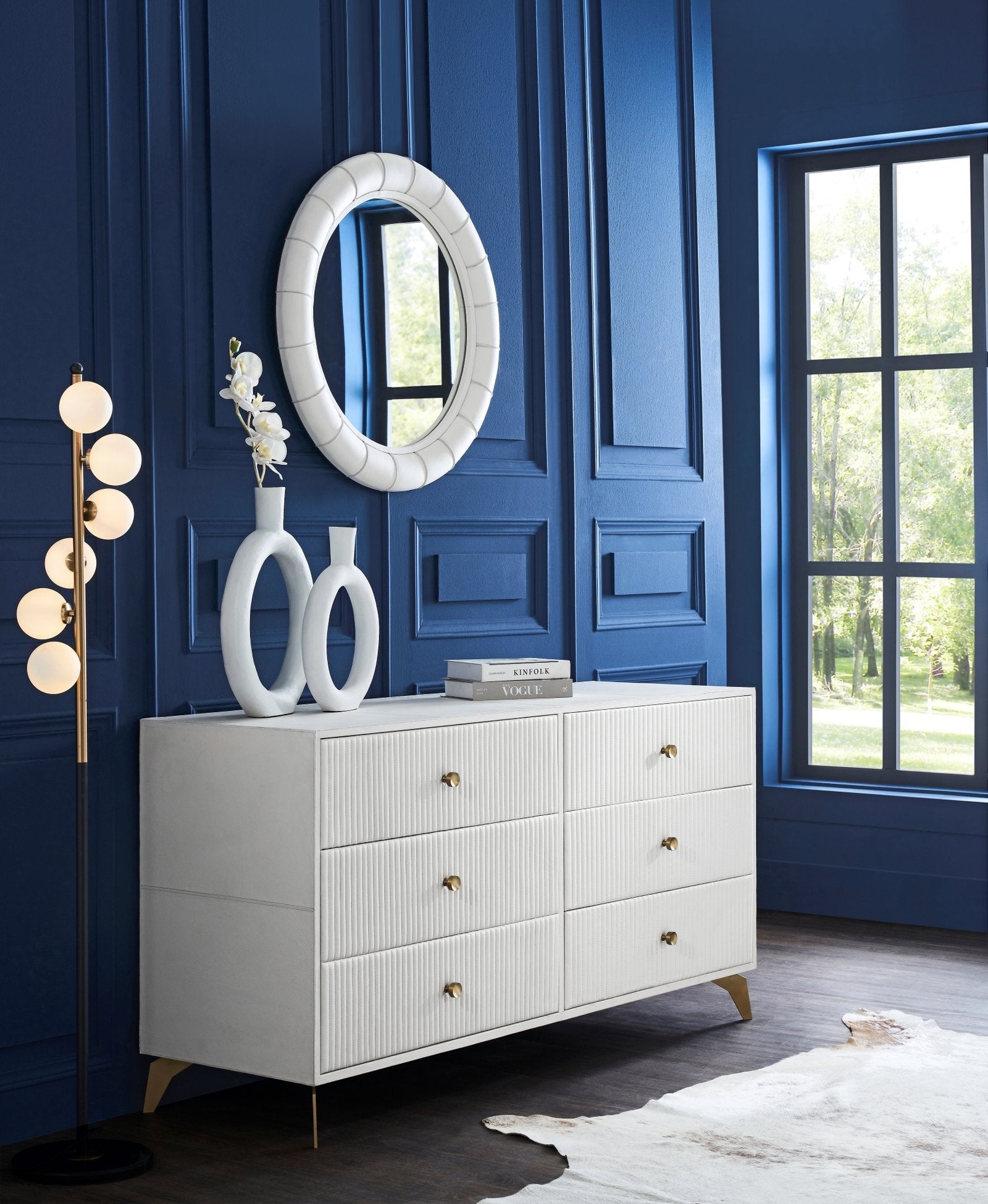 FN-5203-642033_1|White leather ridged dresser with gold pulls, a modern lamp, and mirror in a blue paneled room, luxury furniture.