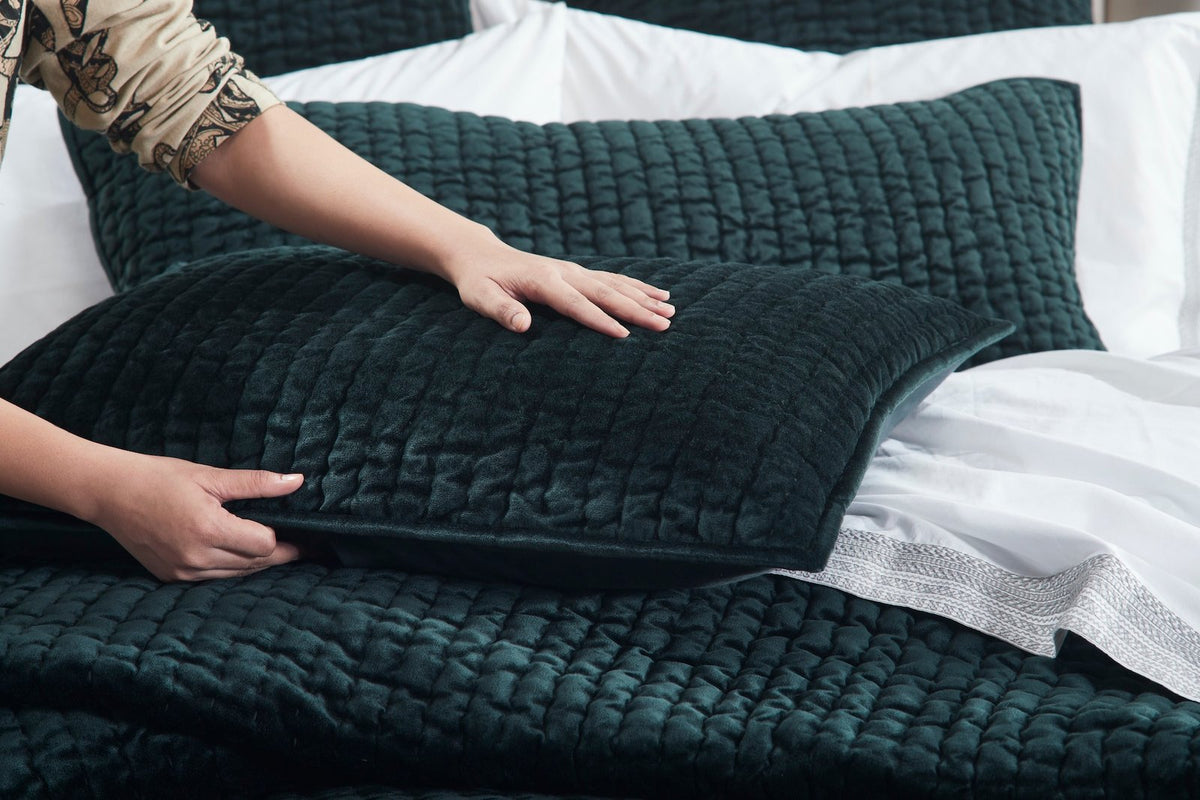 QT-363-11096_5|Hand adjusting a plush forest green quilted pillow, emphasizing its soft, textured design for ultimate bed comfort.