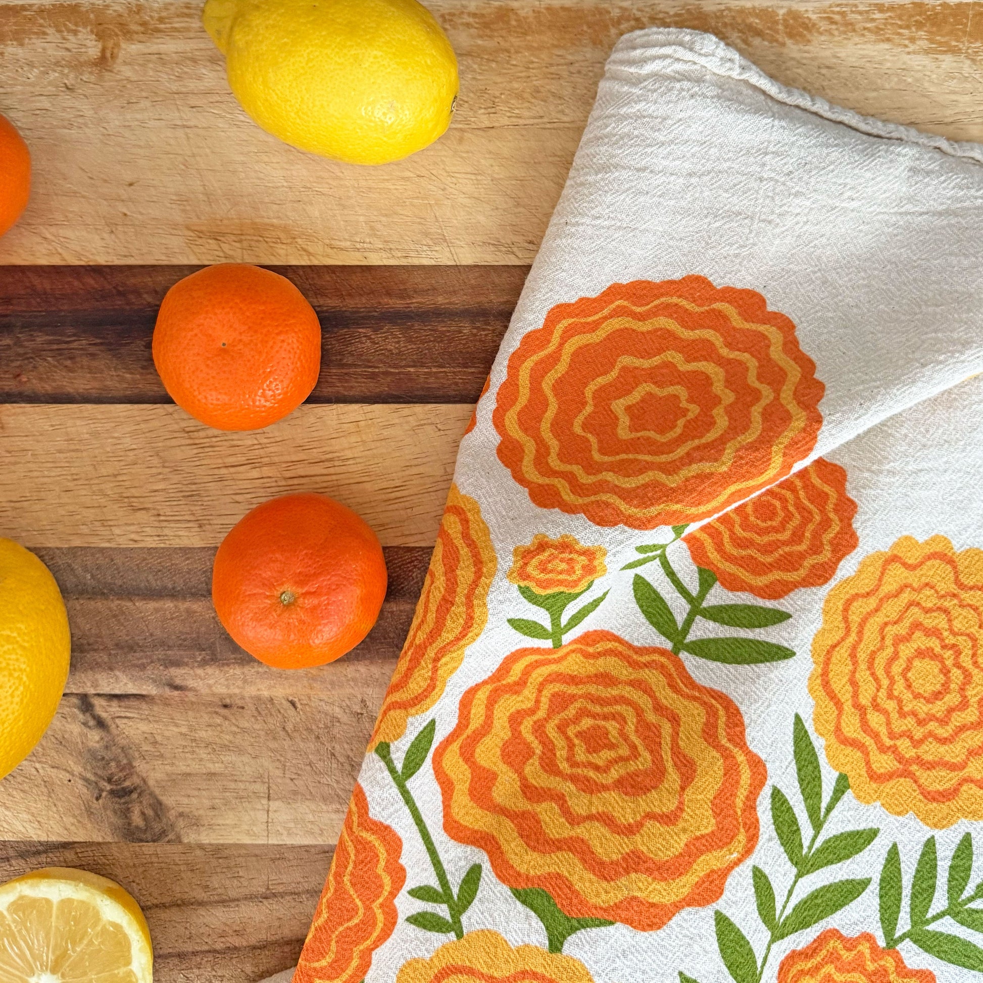 Marigold dish towel laid next to oranges and sliced lemons on a cutting board.