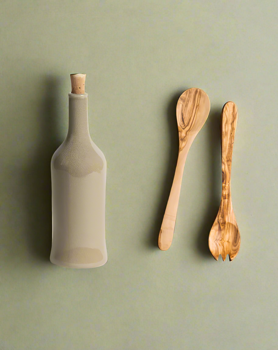 A handcrafted olive wood salad server set accompanied by a stoneware bottle, both displayed against a neutral background.