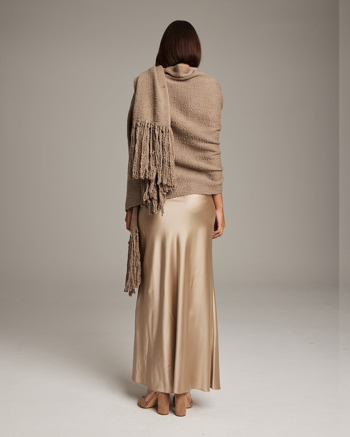 Model wearing a Flammé Fringe Wrap in a neutral color, showcasing the fringe detail.