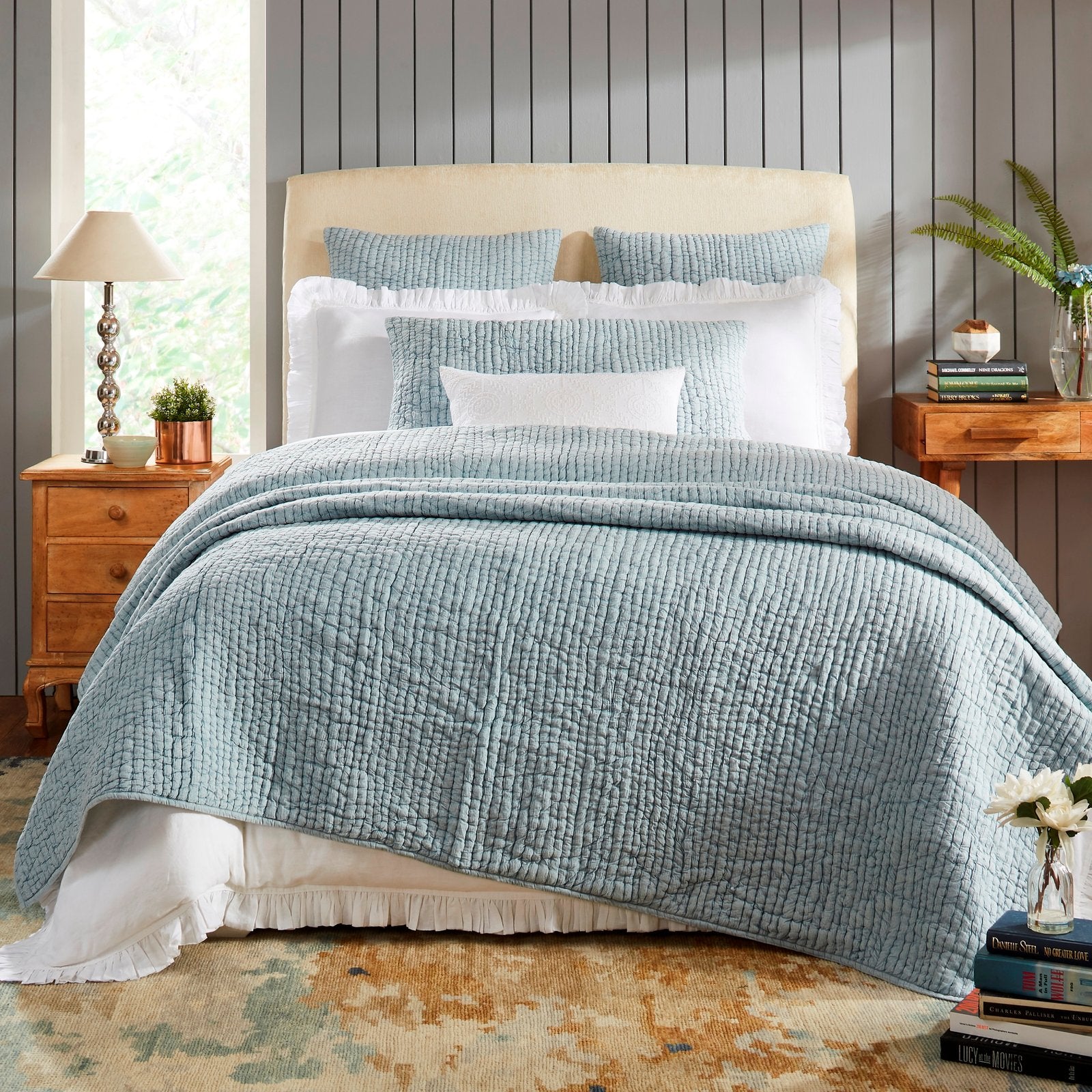 QT-316-X_1|Inviting bedroom with a blue quilted bedspread, white ruffled bed skirt, neutral headboard, and wooden nightstands.