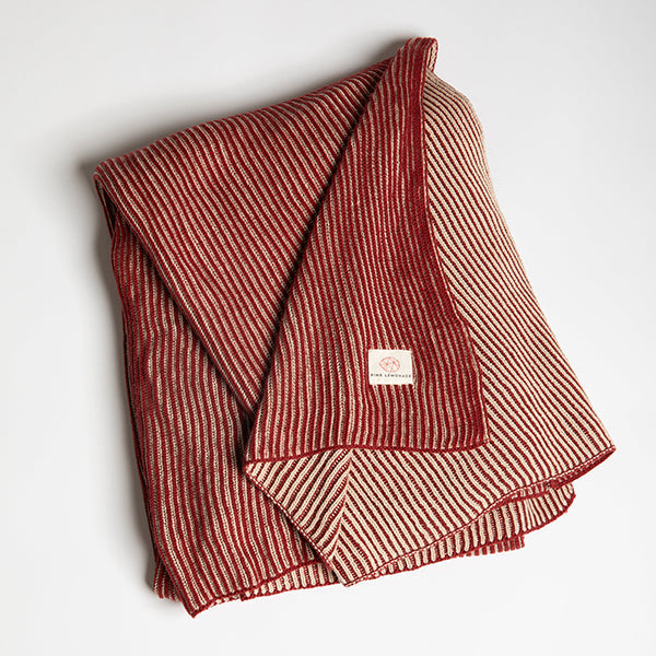 Folded red and white striped textured blanket photographed on a light gray background.