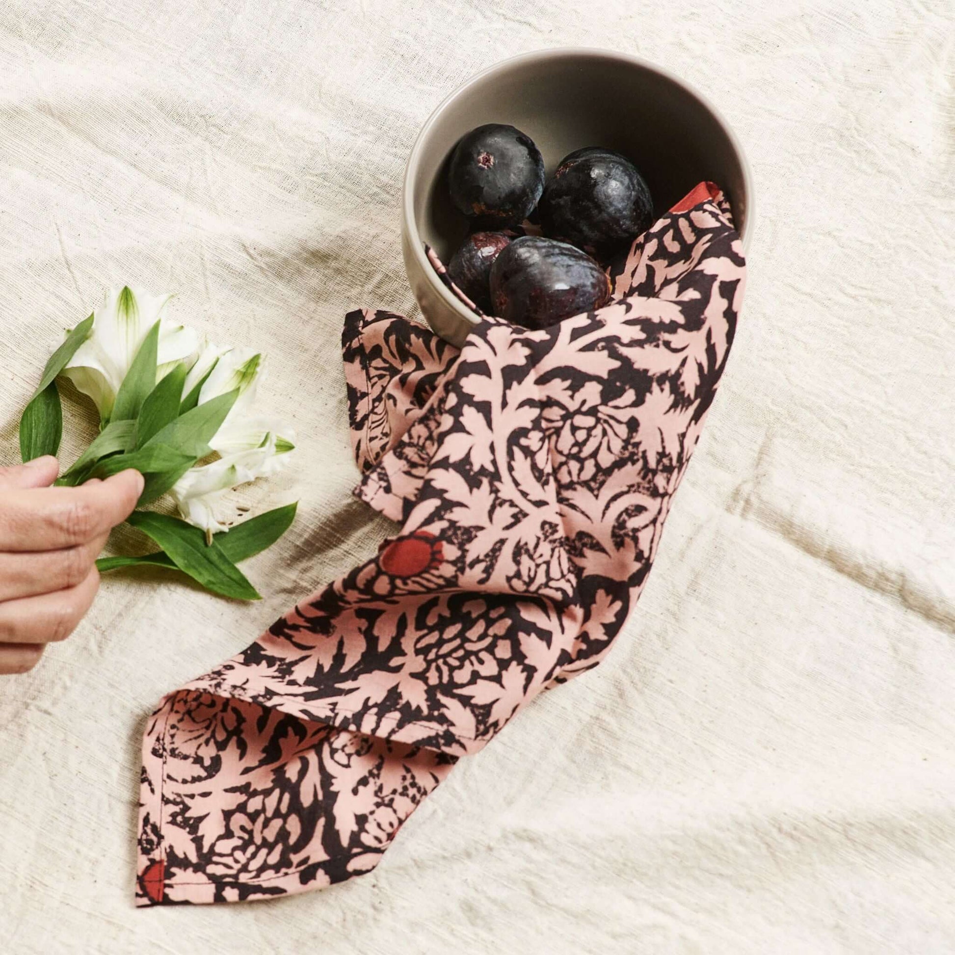 Hummus Floral Wax Block Printe Cotton Table Napkin( set of 4 ) elegantly draped with a bowl of plums and flowers.