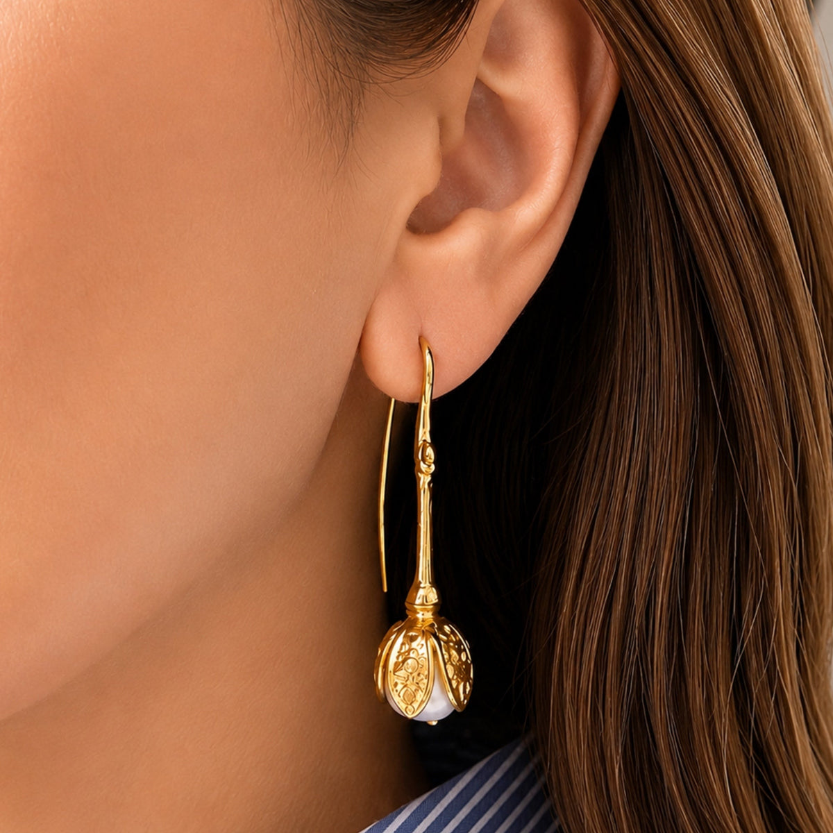 A close-up of a woman's ear wearing a gold tulip design pull-through earring a white pearl inlay.