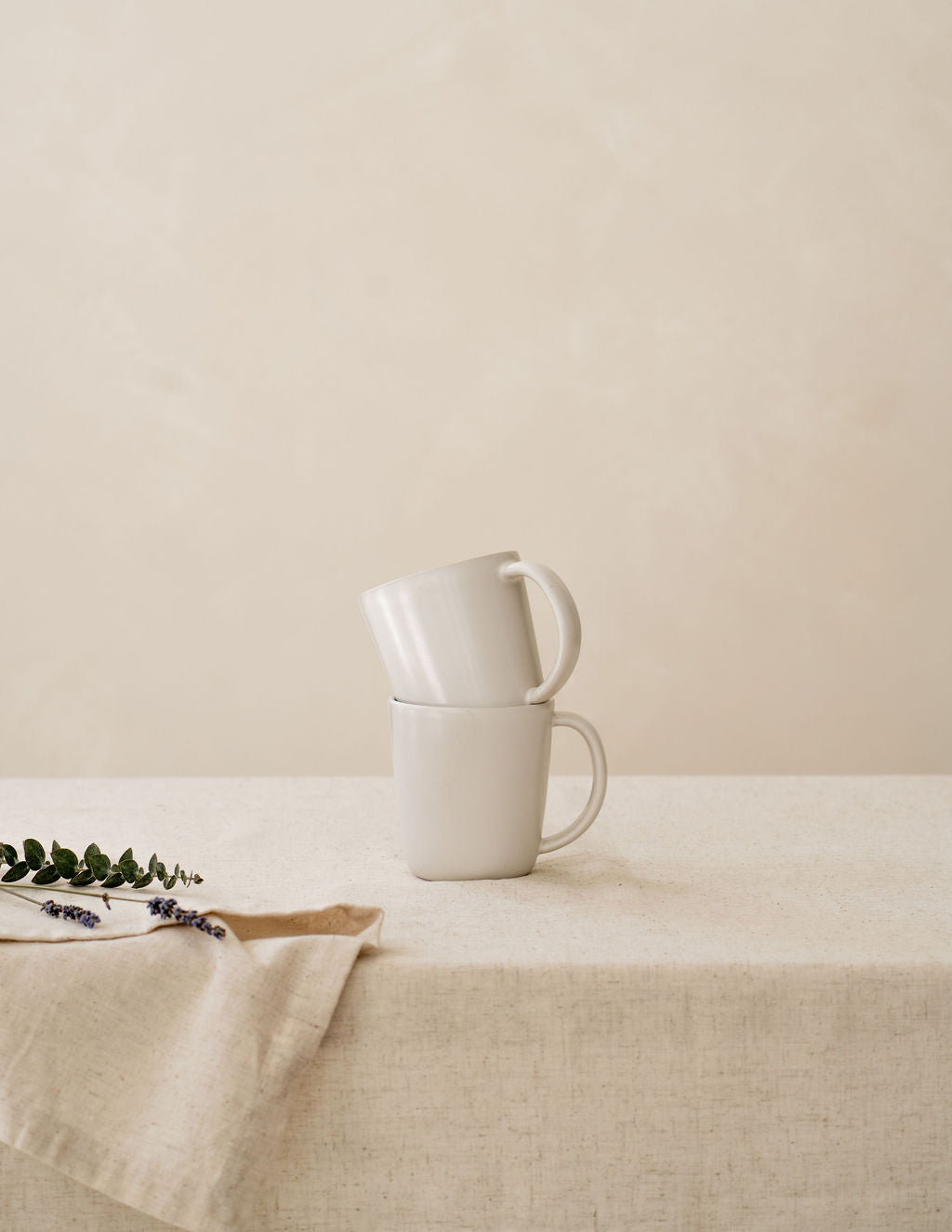 Stacked Bone ivory ceramic mugs by Hamkke Home on a neutral linen table.
