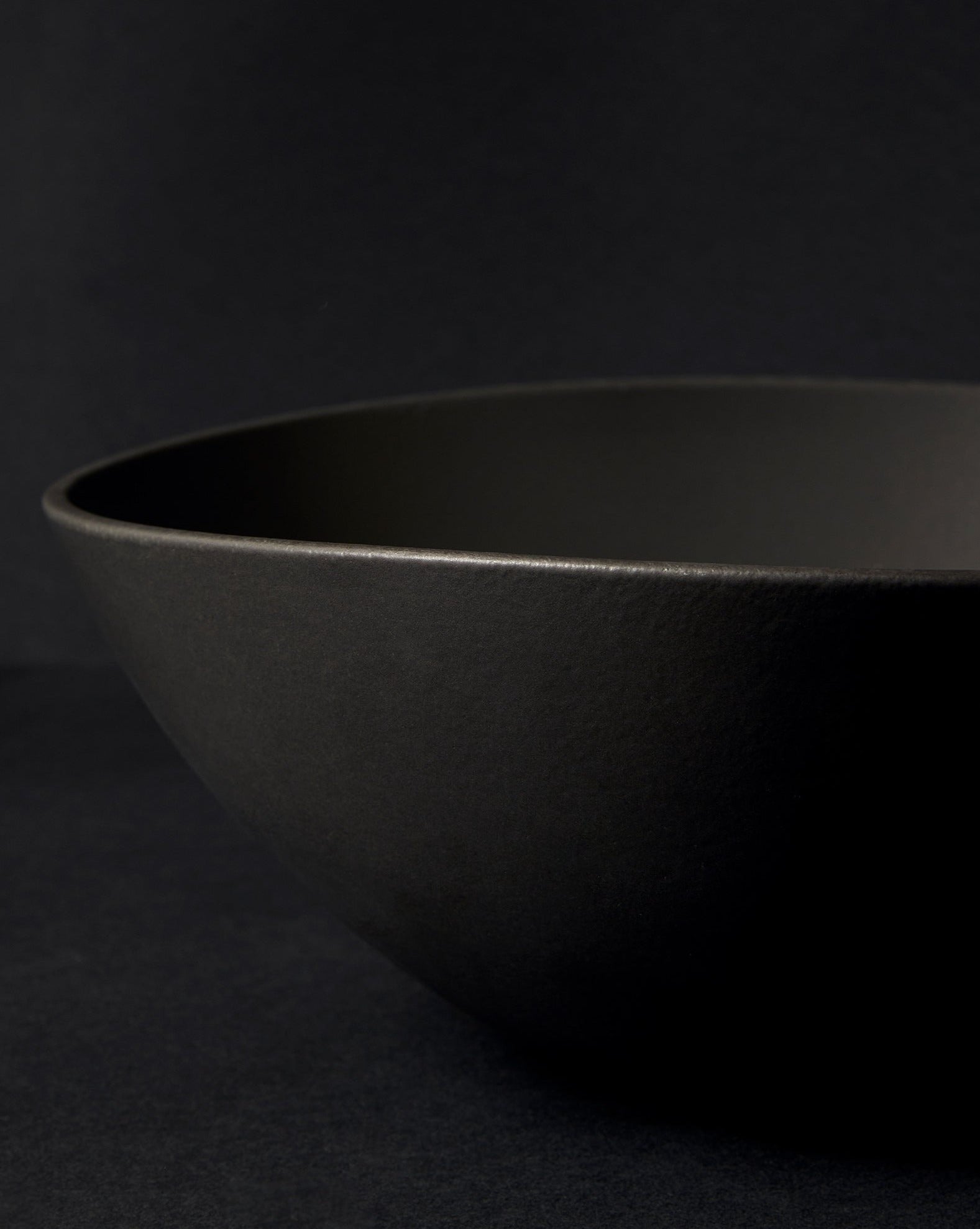 Partially captured black stoneware serving bowl with the 'GHARYAN' logo visible, set against a black background.