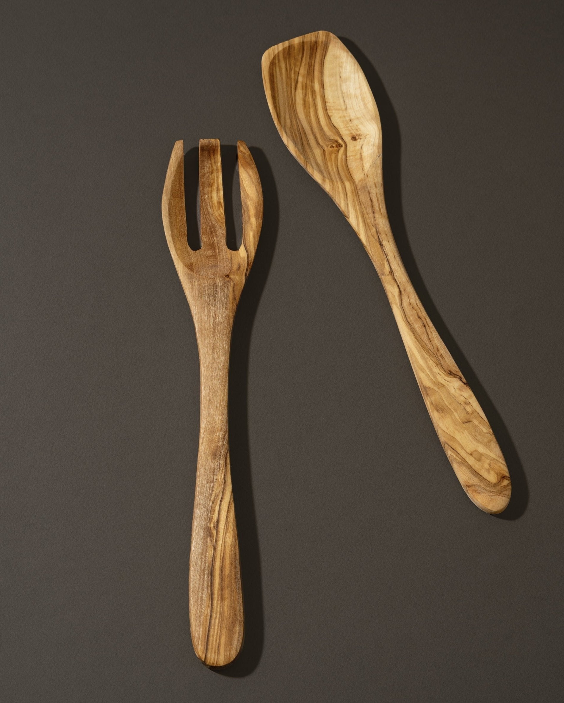 A wooden spoon and fork set made of olivewood, displayed against a dark background. 