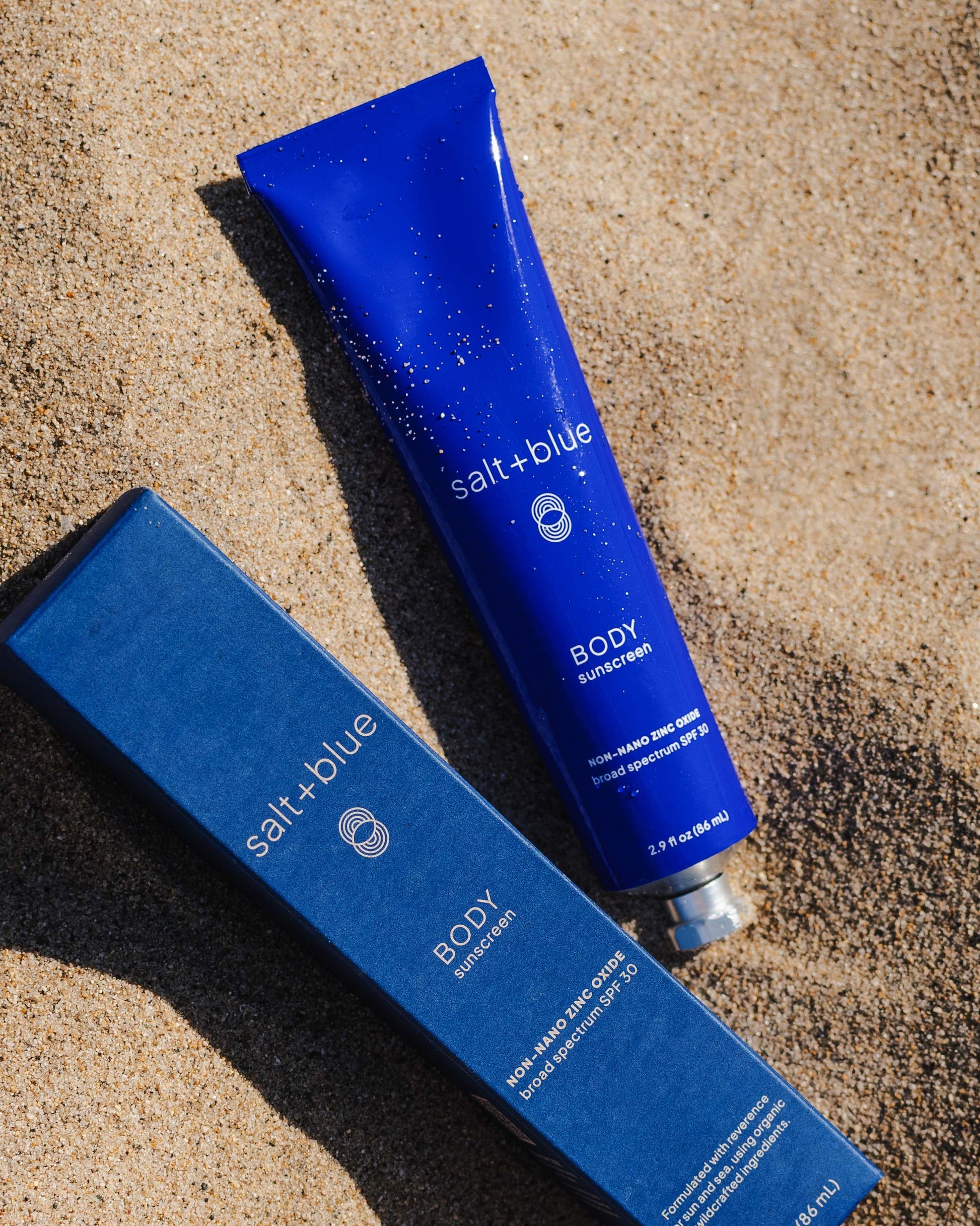 salt+blue sunscreen tube and box on sand