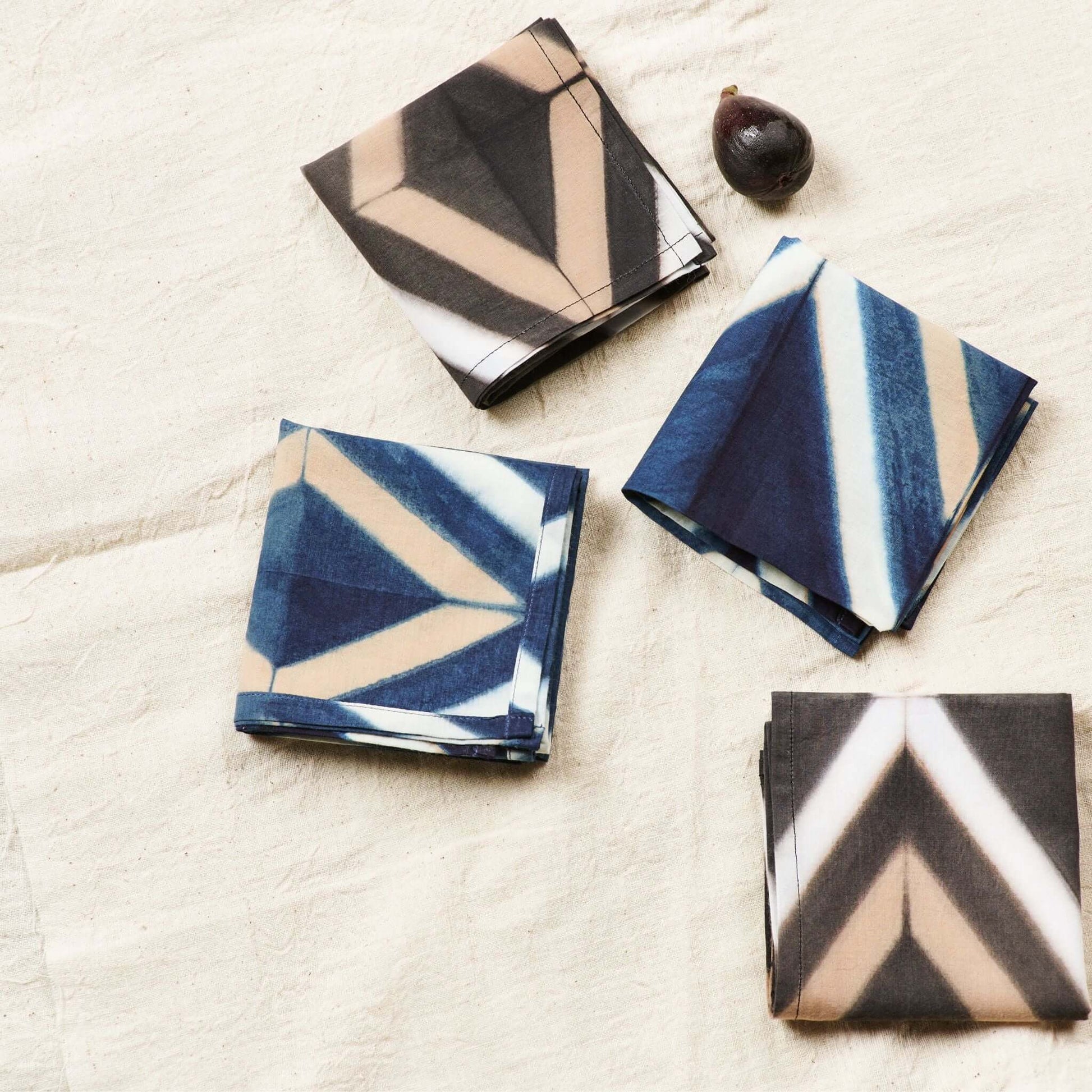 Tisa Indigo Hand Crafted Shibori Print Cotton Table Napkin set of 4 displayed on a textured surface with a fig.