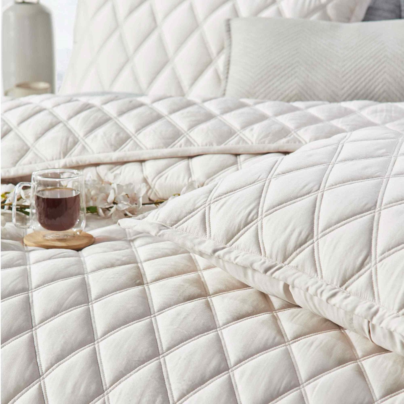 CL-180-11096_4|Cream diamond-quilted coverlet with elegant sheen, perfect for luxury bedding. Accentuated by a warm cup of tea.