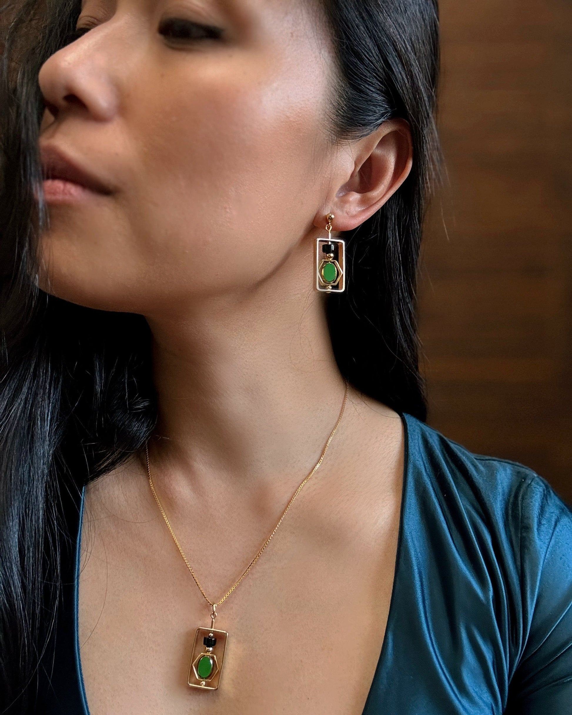 Woman wearing gold earrings and necklace with green gemstones against a dark background