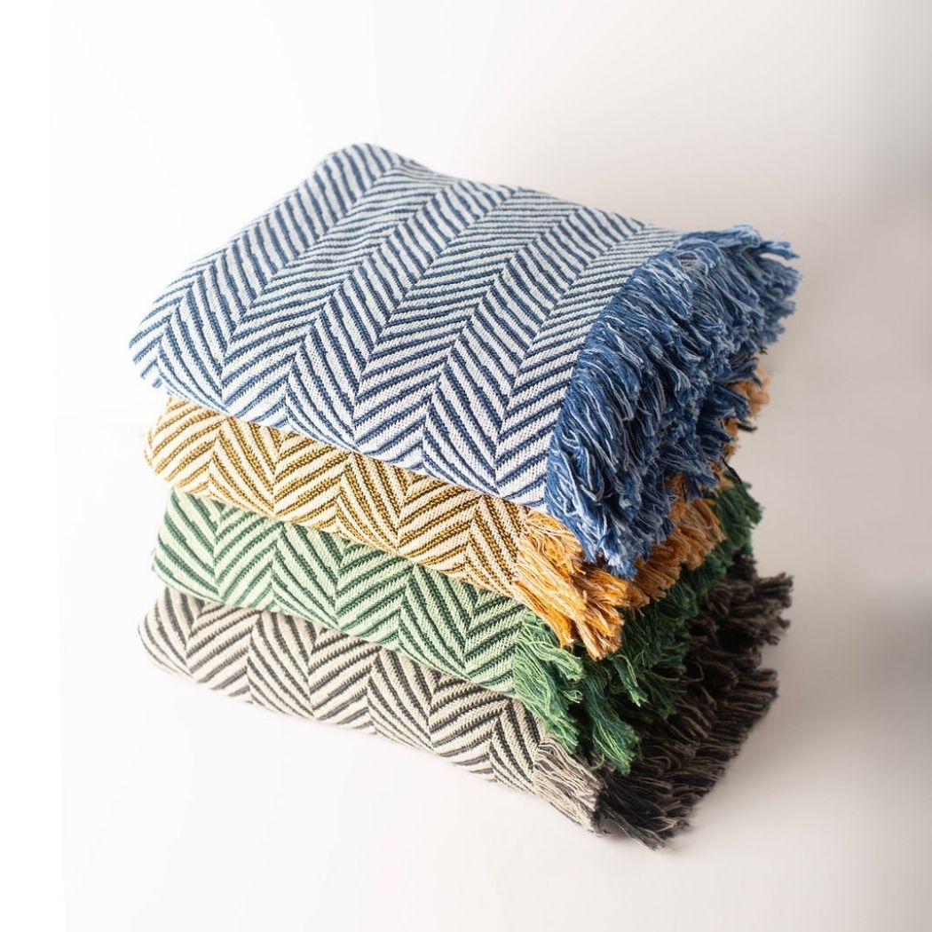 Stack of Henry reversible herringbone woven throw blankets in blue, gold, green, and neutral colorways