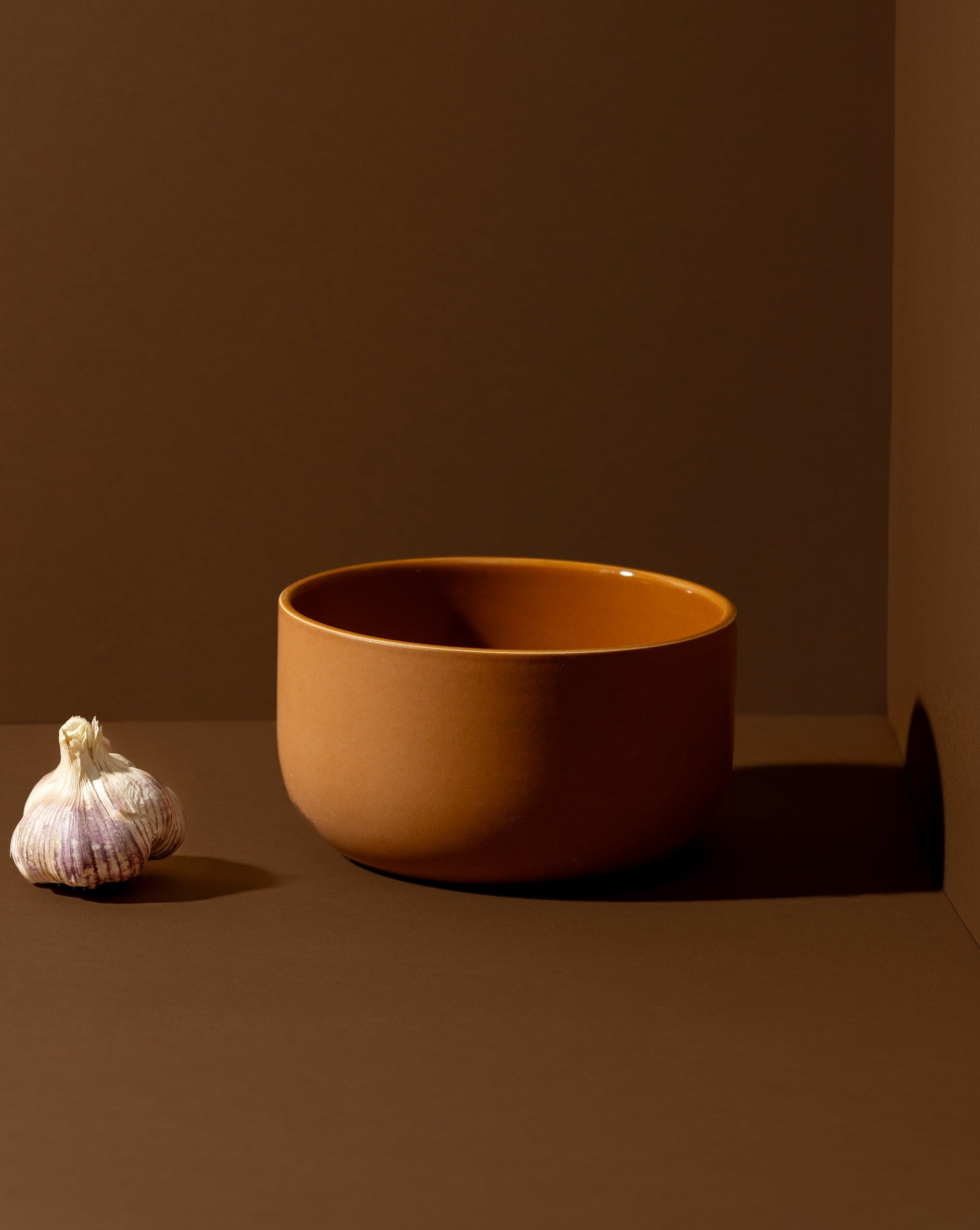 Terracotta-colored stoneware bowl with a whole onion placed beside it.