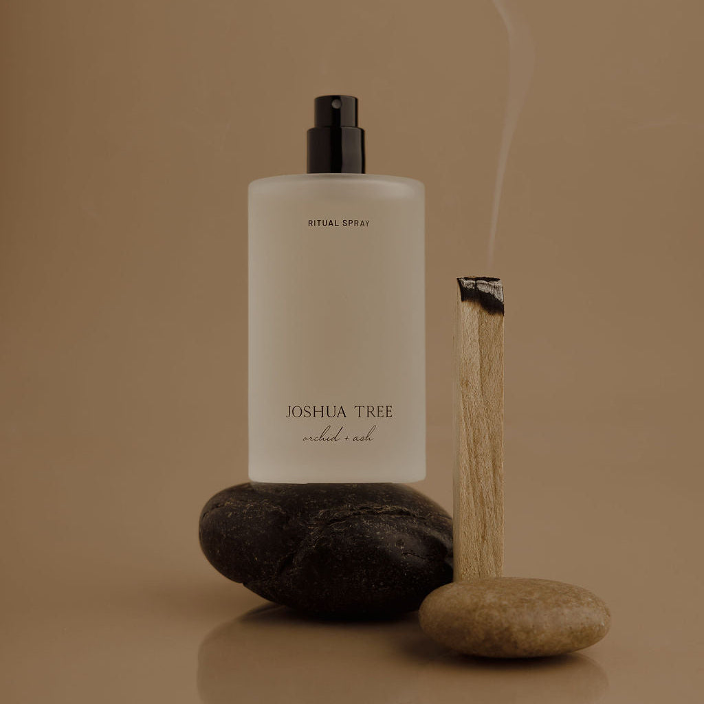 White bottle with black cap labeled 'Joshua Tree' on a reflective surface with stones and smoke on a beige background