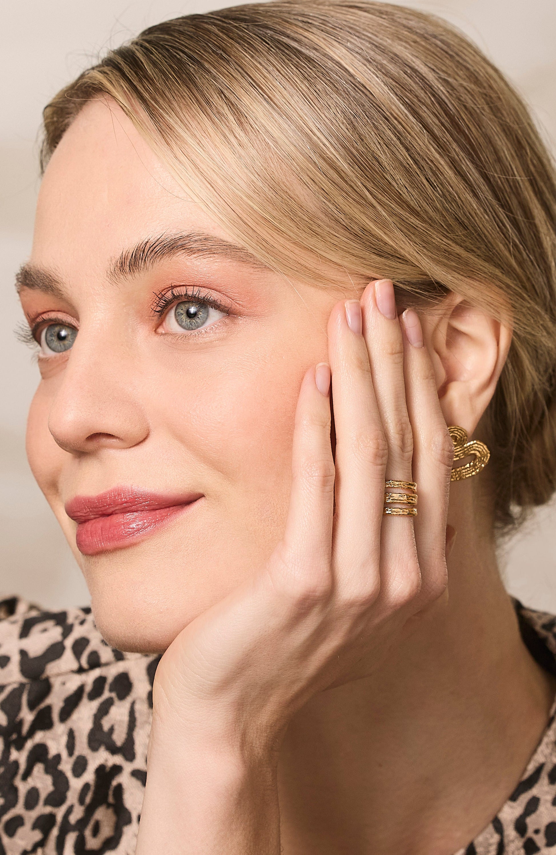 Model wearing a gold ring and textured earrings. 