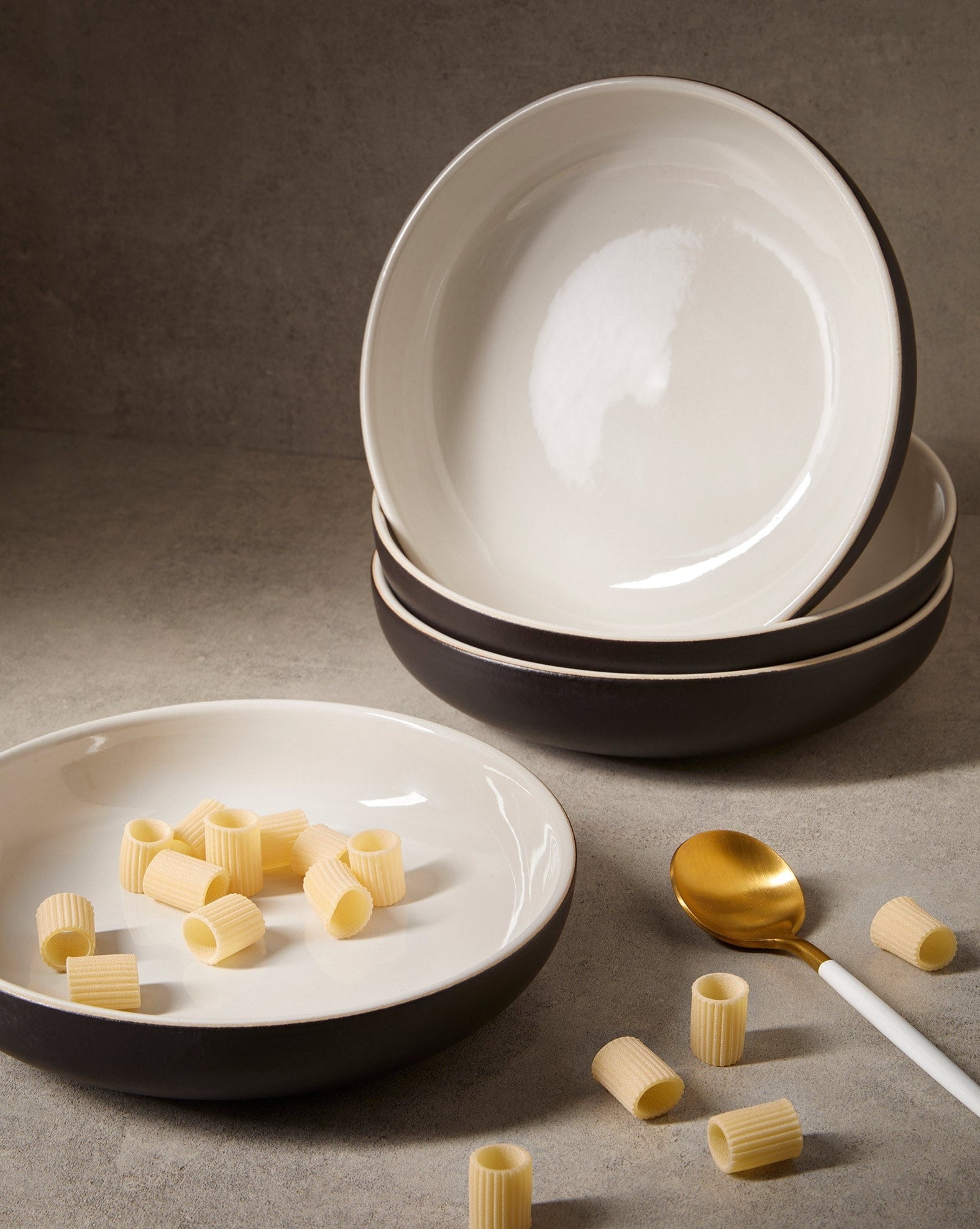 A set of white stoneware pasta plates with a matte finish, including a serving suggestion with pasta on one of the plates, displayed on a neutral background.