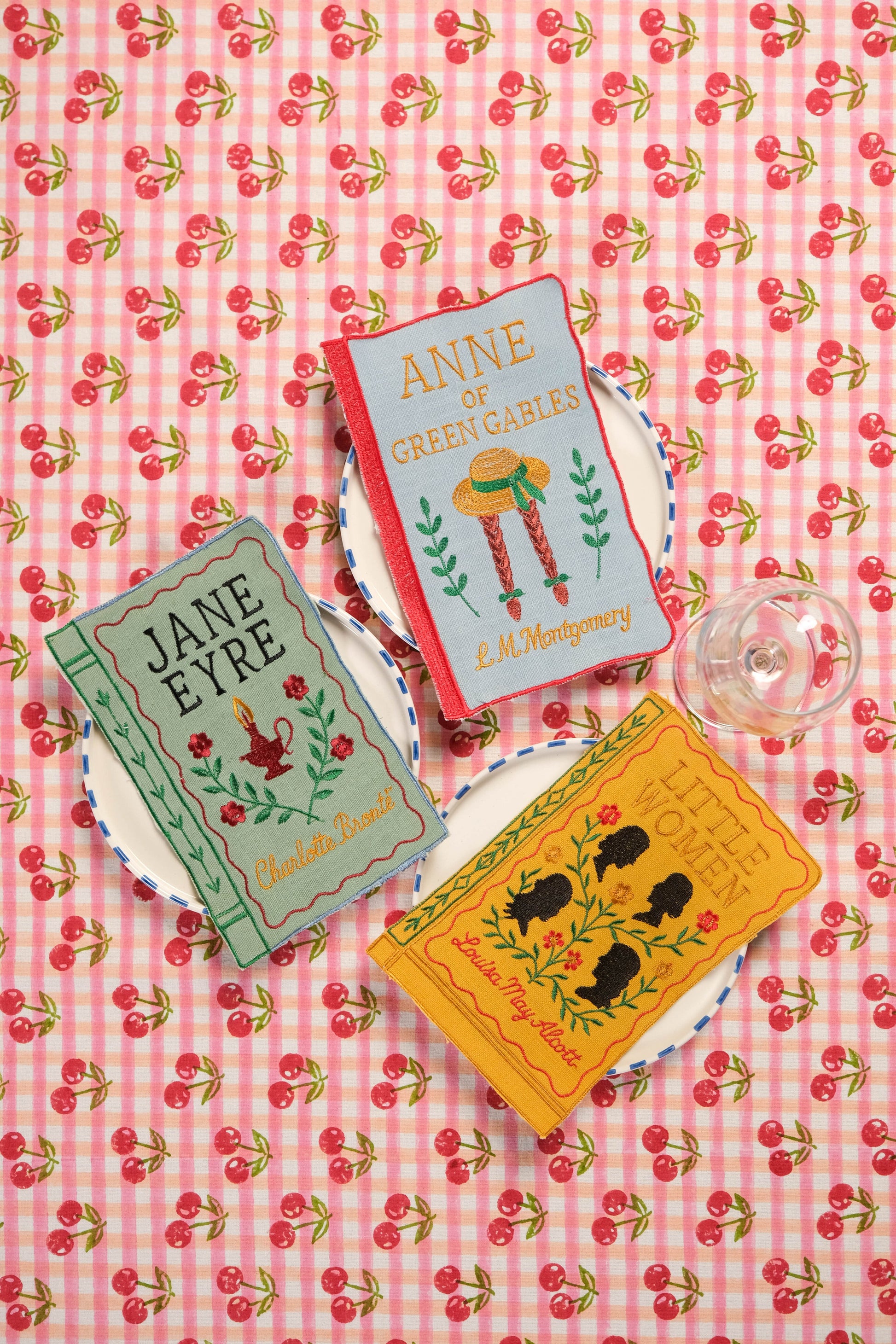 Literary book embroidered napkins set displayed on cherry patterned tablecloth with plates